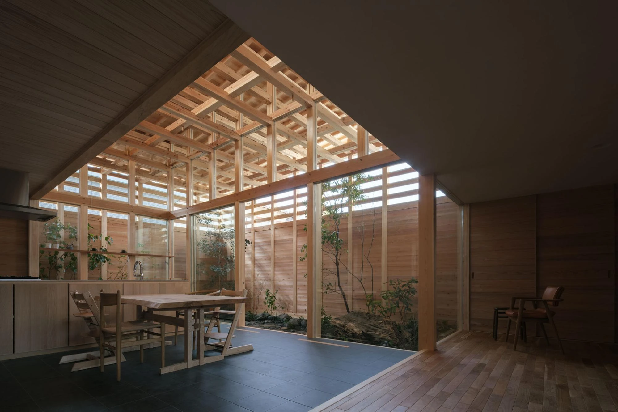 Single Family House in Aichi by Ryota Sekiya, photographed by Shun Fukuda — the dining-kitchen under a solid ceiling opens through the beam lattice to a planted void, slate-tile and oak floors below.