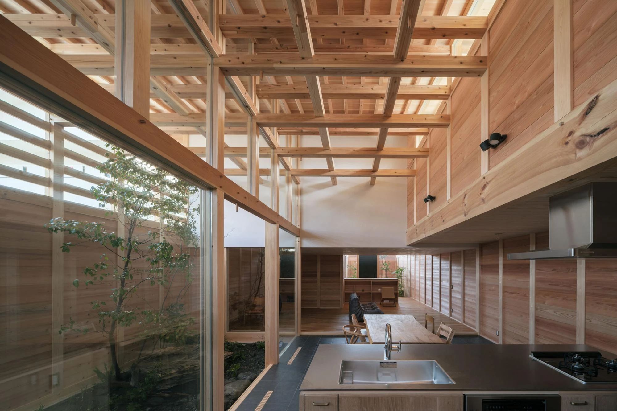 Single Family House in Aichi by Ryota Sekiya, photographed by Shun Fukuda — a view along the kitchen toward the living area, low light raking across cedar boards and the deep coffered lattice overhead.