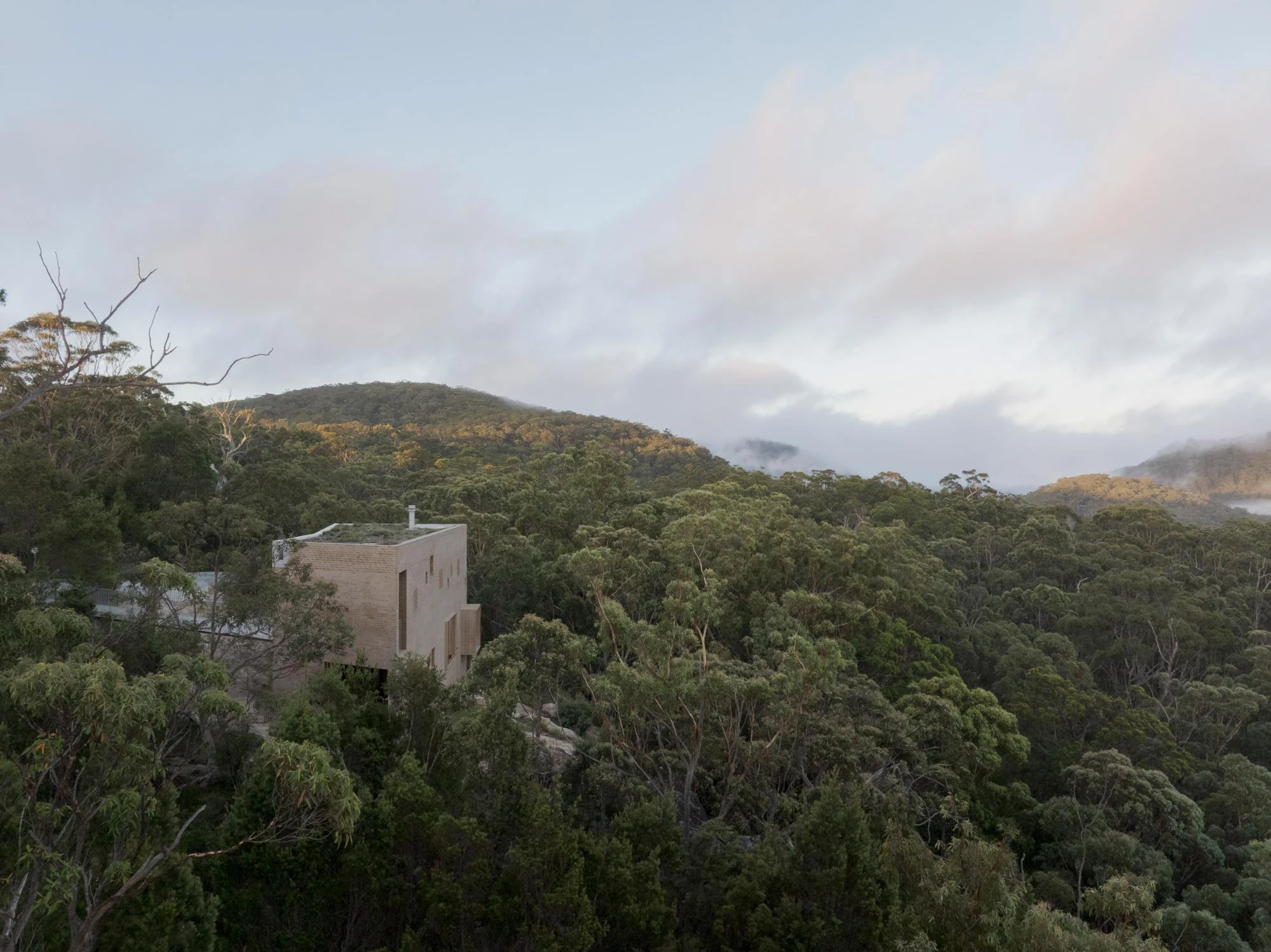 EA House, Southern Highlands by Bokey Grant, photographed by Clinton Weaver, the house stands above the treetops on the escarpment, forested ridgelines and cloud stretching behind it.