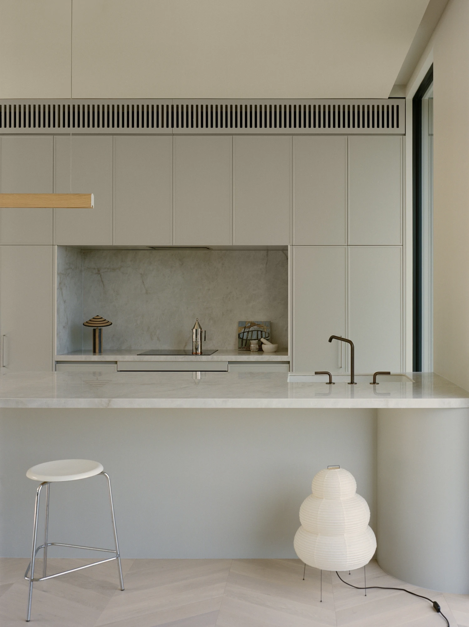 Cathedral House by JAK Architecture, photographed by Tasha Tylee — a detail of the kitchen with a marble splashback and benchtop, aged brass tapware, herringbone timber floor and a white paper lantern lamp.