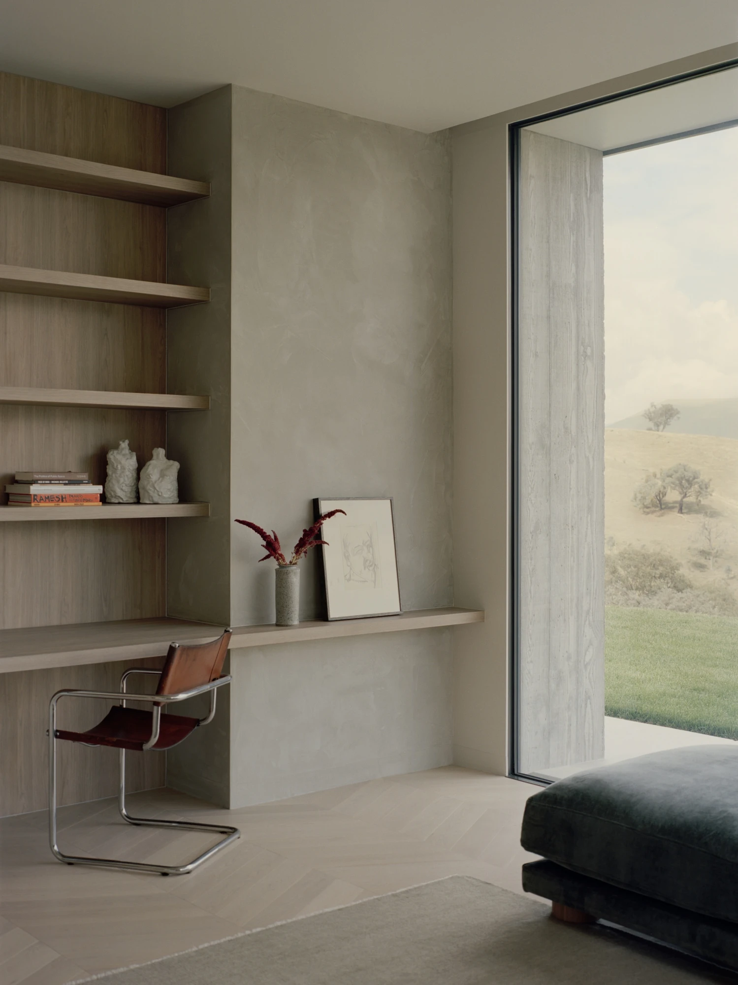 Cathedral House by JAK Architecture, photographed by Tasha Tylee — a study corner with a polished plaster wall, floating oak shelves and desk, a tan leather cantilever chair and a full-height window onto the hills.