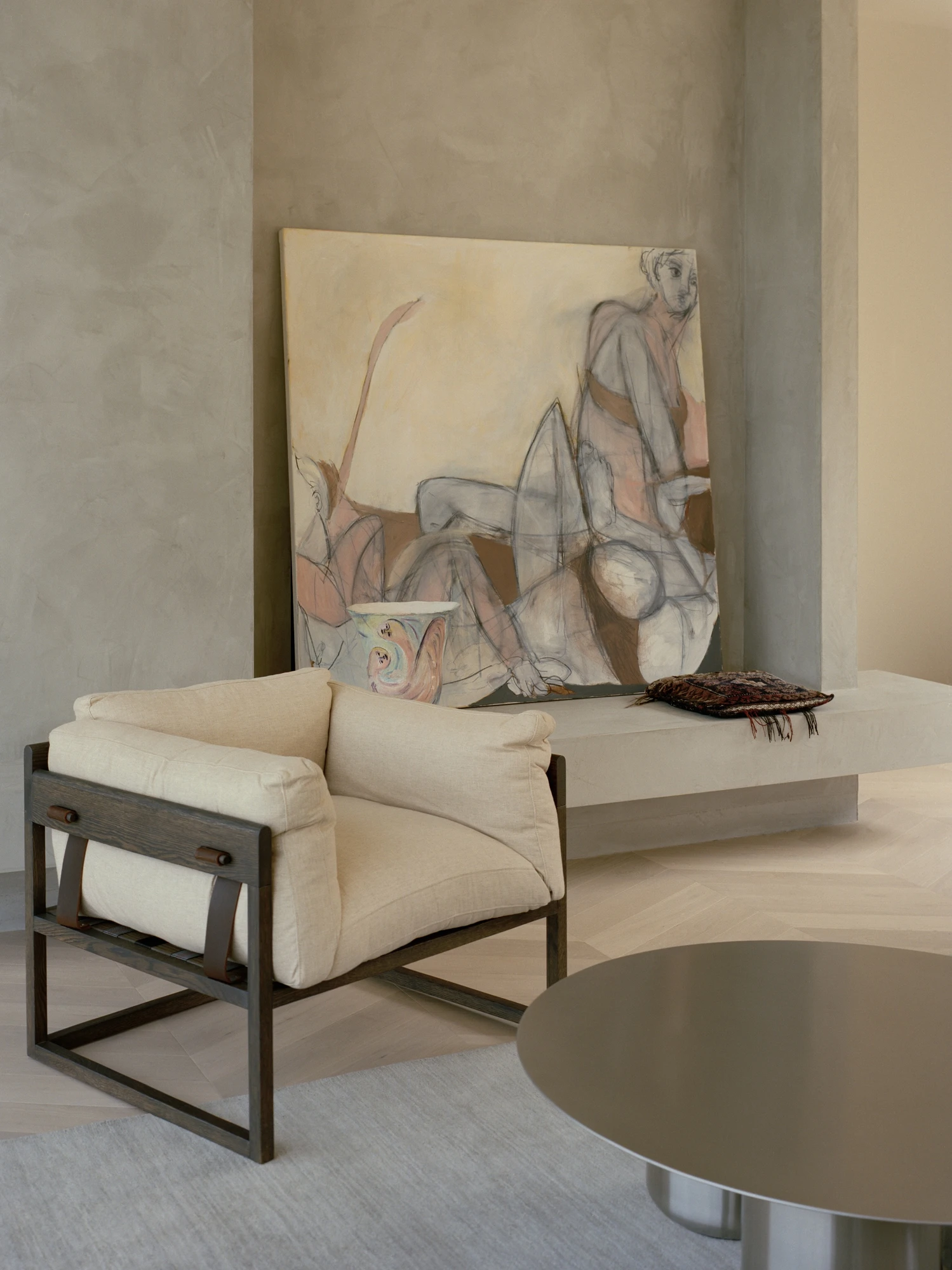Cathedral House by JAK Architecture, photographed by Tasha Tylee — a linen armchair on a dark timber frame set before a large figurative canvas leaning on a polished plaster wall above a low bench.