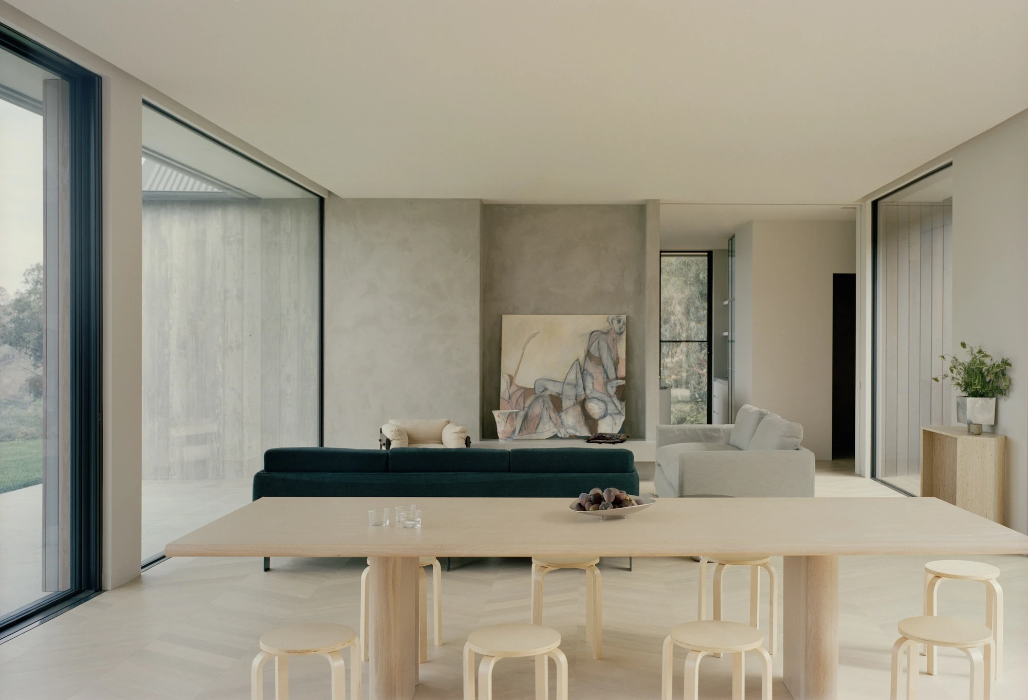 Cathedral House by JAK Architecture, photographed by Tasha Tylee — an open living and dining space with a polished plaster wall holding a large figurative painting, a dark green sofa and pale timber table on a herringbone floor.