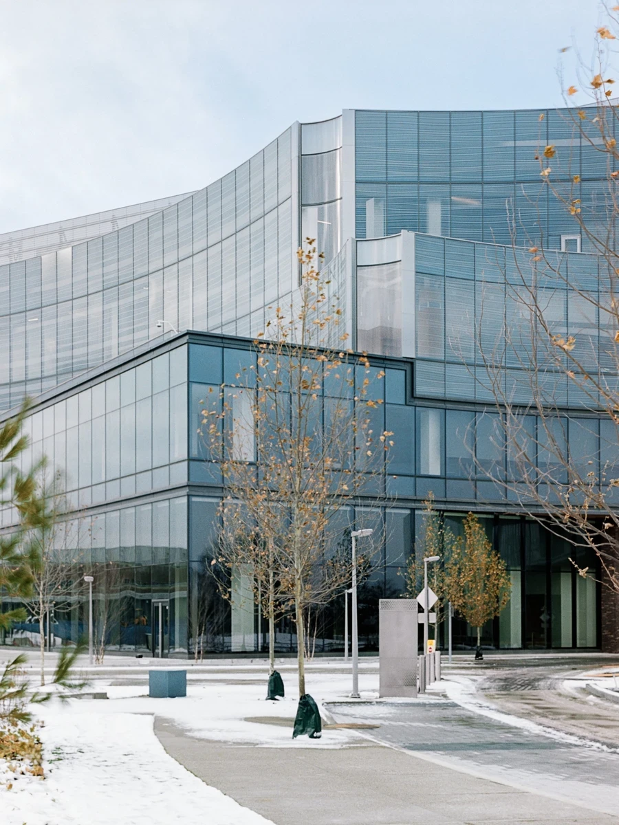 Ford World Headquarters by Snøhetta, photographed by Aaron Feliciano — a detail of the fritted glass corner where the curtain wall meets the wood soffit and a slender concrete column.