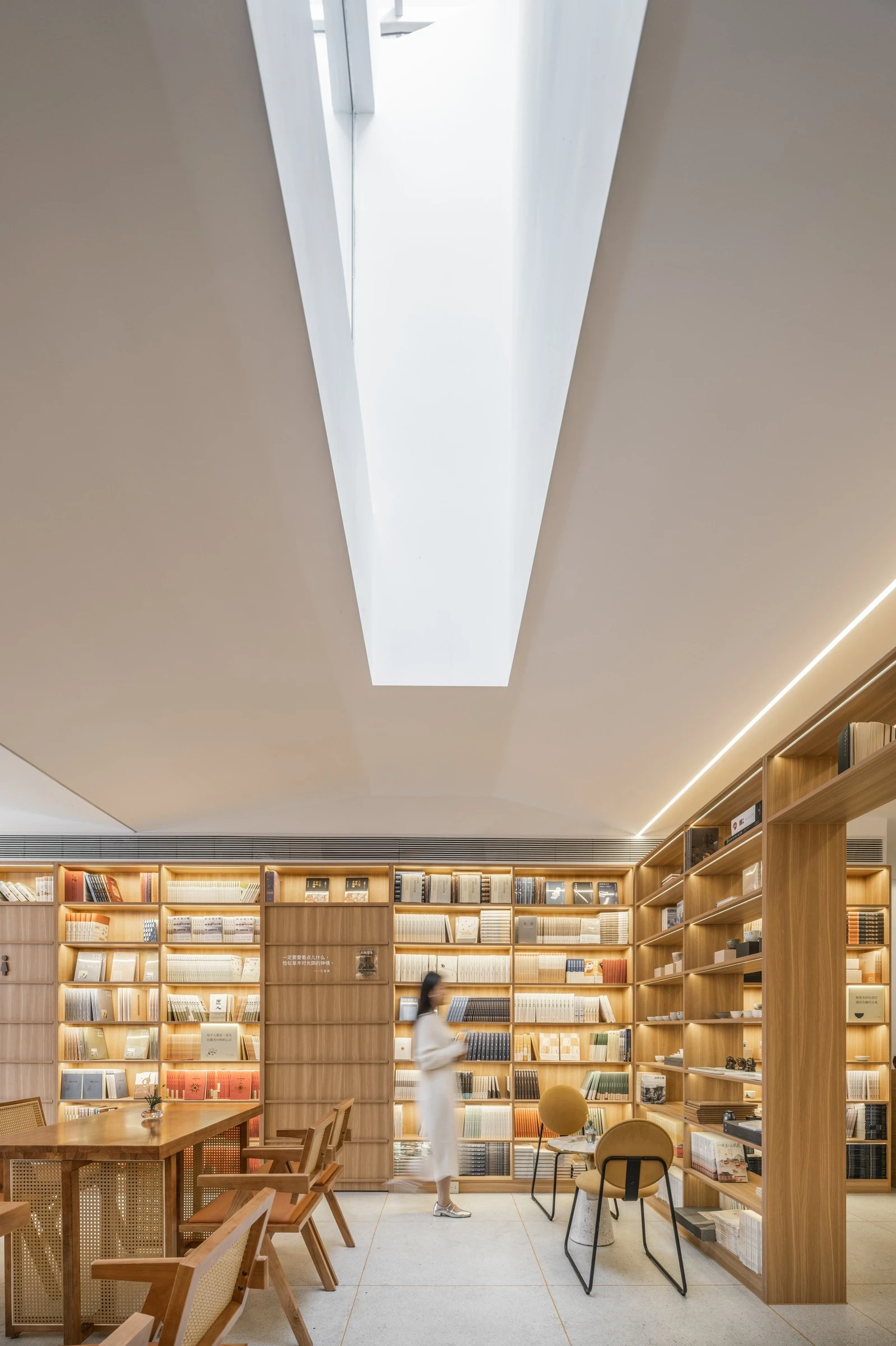 Heart Fields by Wutopia Lab, photographed by CreatAR Images — a reader sits beneath a skylight where full-height oak shelving follows the pitch of the gabled ceiling.