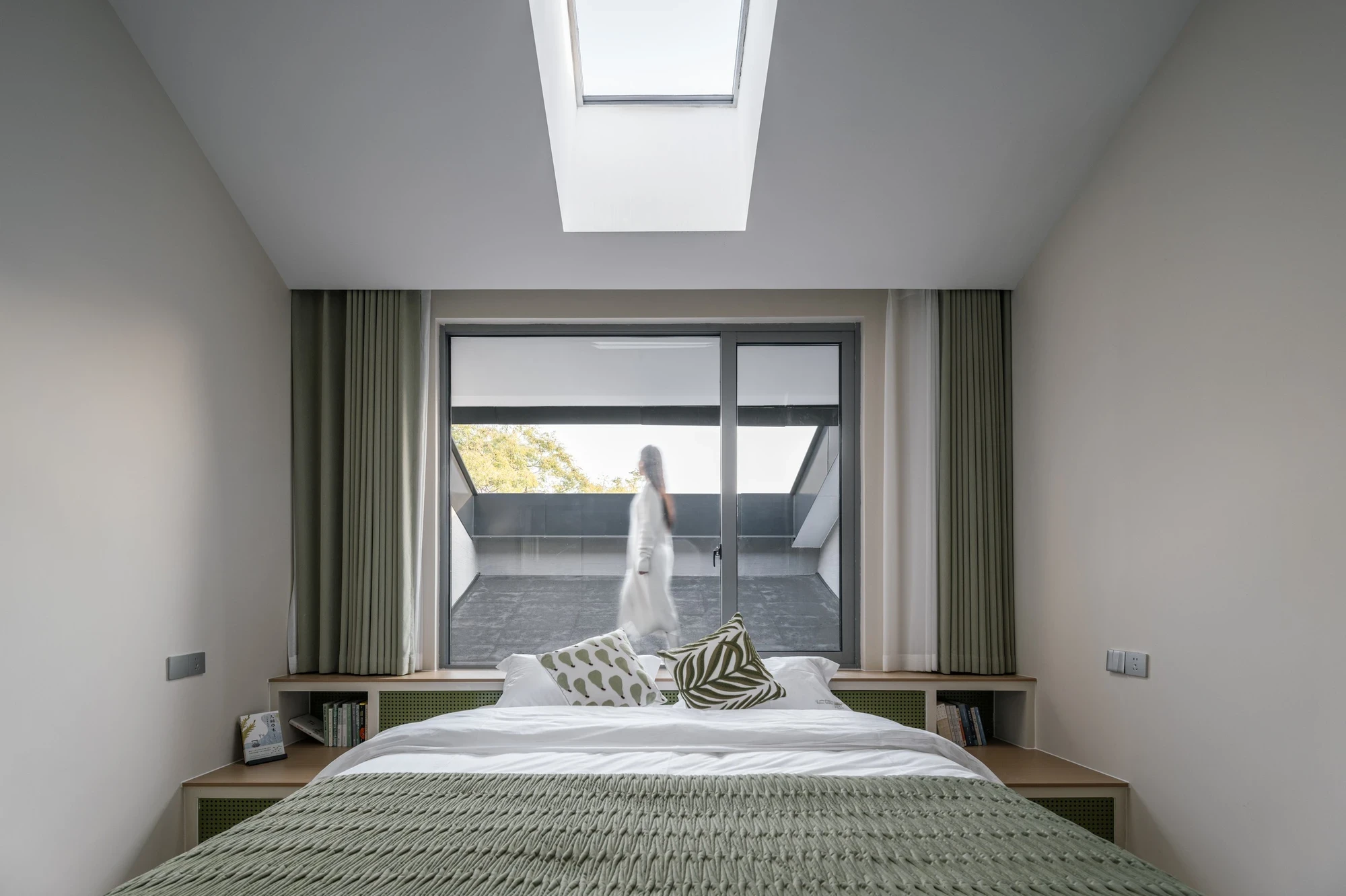 Heart Fields by Wutopia Lab, photographed by CreatAR Images — a guest room with sage-green curtains and a skylight opens through a sliding glass wall onto a roof terrace.