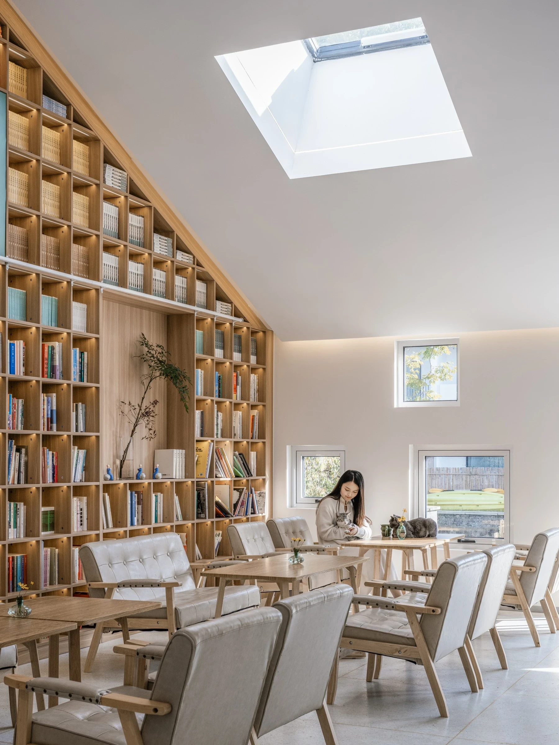 Heart Fields by Wutopia Lab, photographed by CreatAR Images — a long stone counter and faceted pitched ceiling with a skylight open onto oak shelving under the gable.