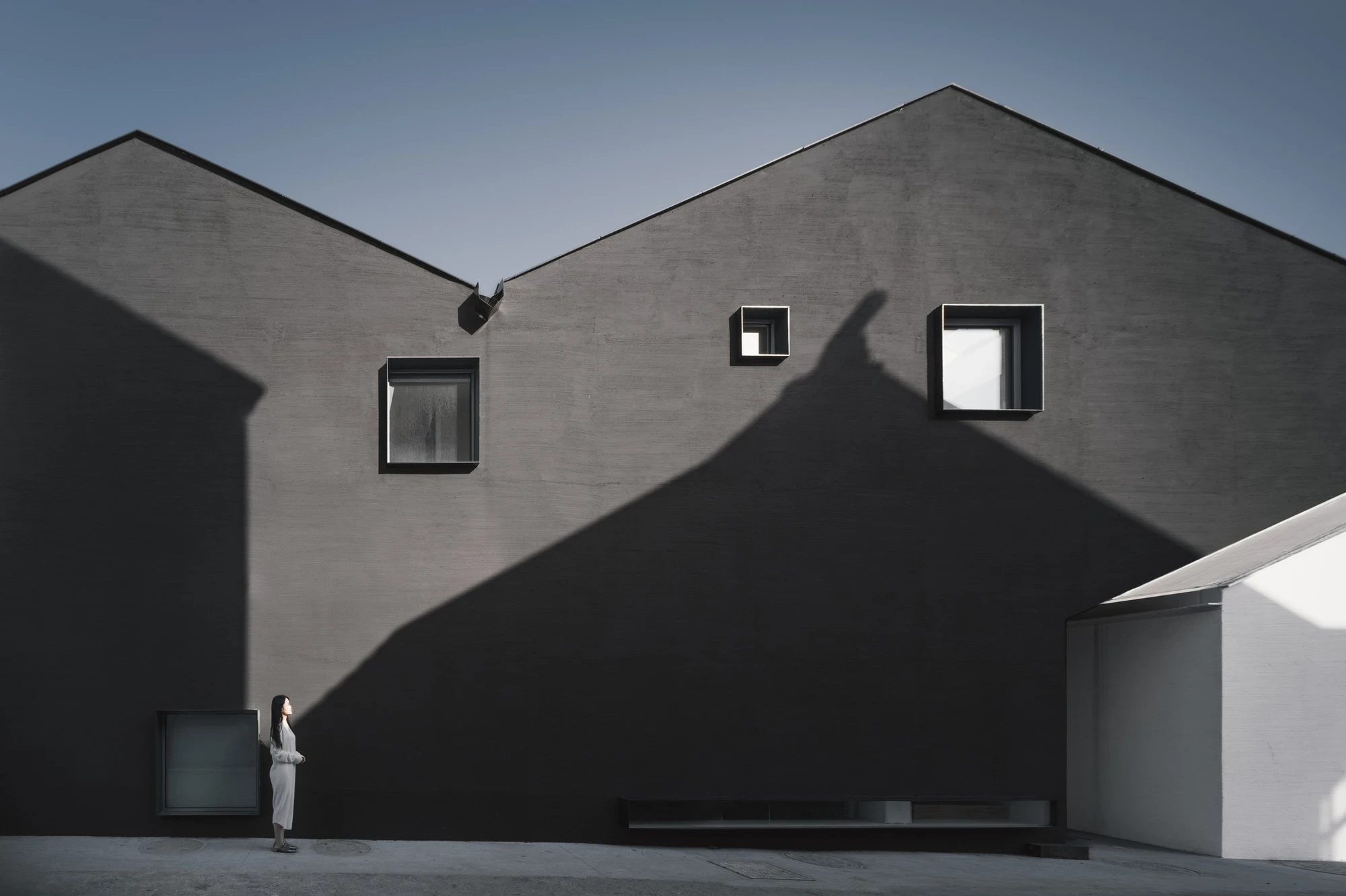 Heart Fields by Wutopia Lab, photographed by CreatAR Images — the whitewashed entrance house presents a symmetrical front of small framed windows and a glazed door beneath a black rooftop volume.