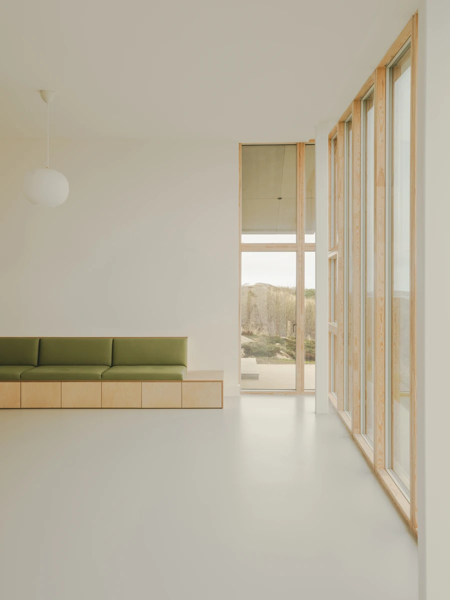 Cruit Island by Pasparakis Friel, photographed by Peter Molloy — a white-walled room where a green upholstered bench sits on birch plywood cabinetry beside a wall of timber-framed glazing.
