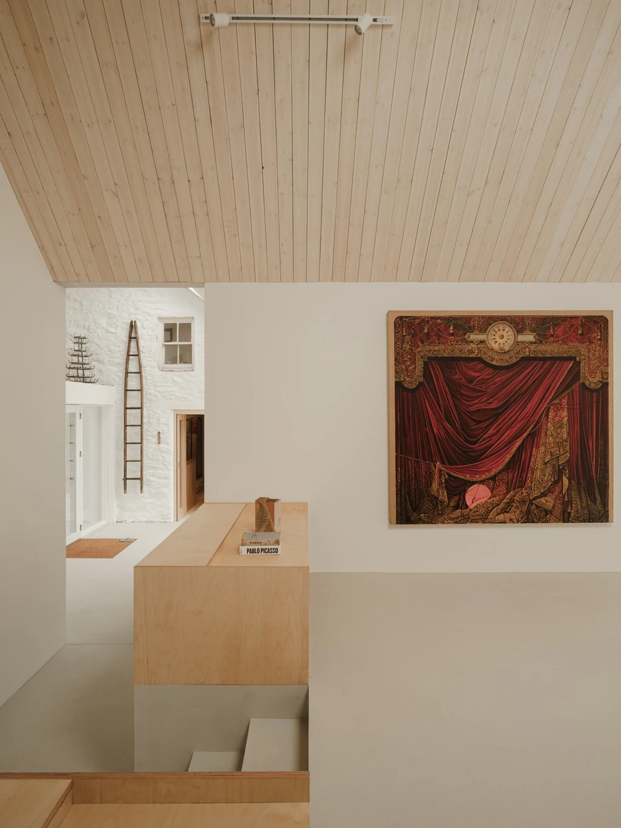 Moss by Pasparakis Friel, photographed by Peter Molloy — a pale timber-lined ceiling slopes over microcement steps and a plywood bookshelf beside a large red-curtain painting.