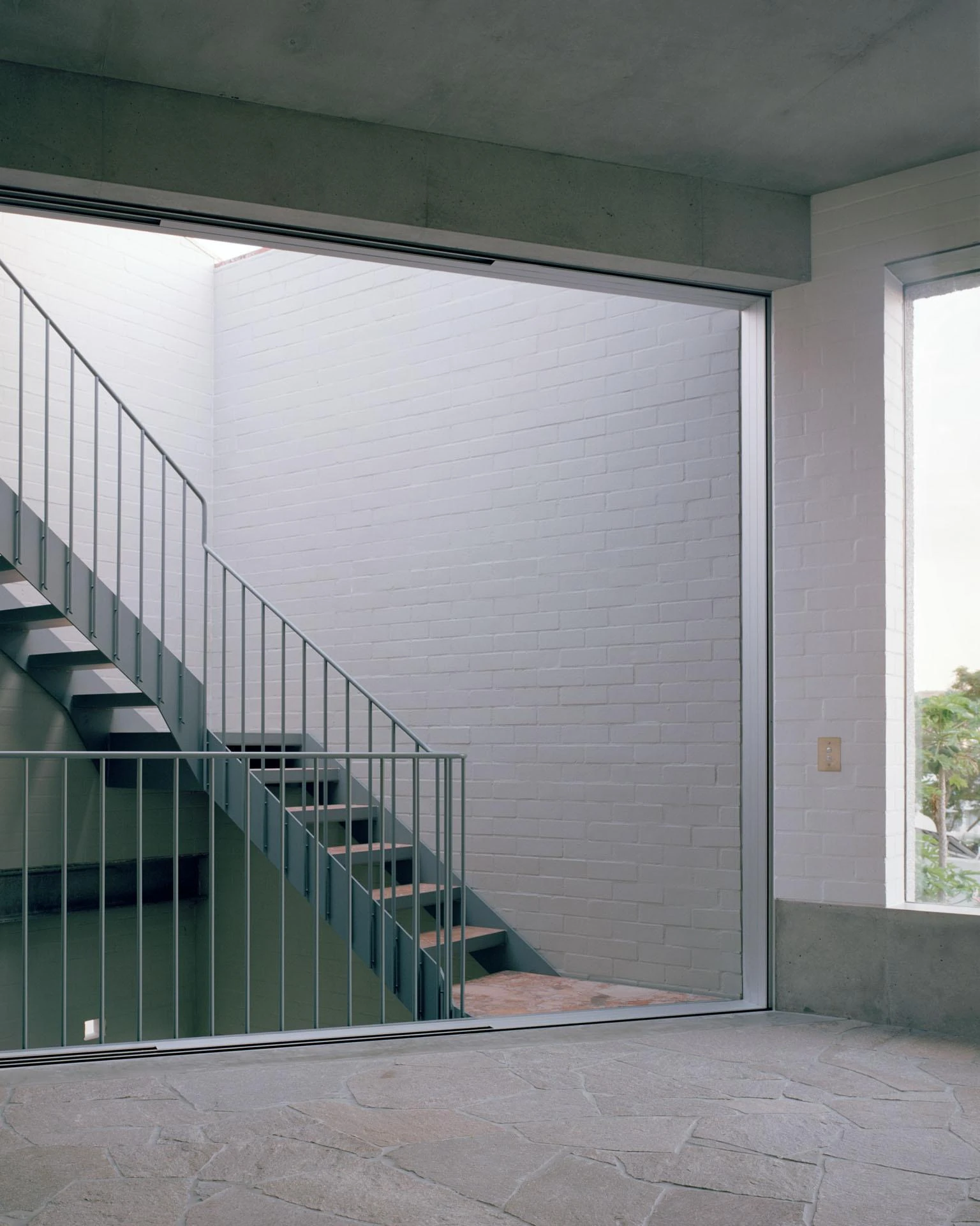 House next to Taylor Square by Anthony Gill Architects, photographed by Rory Gardiner with Colby Vexler — Living level opening to a blue-grey steel outdoor stair, stone-flagged terrace and white painted brick beyond.