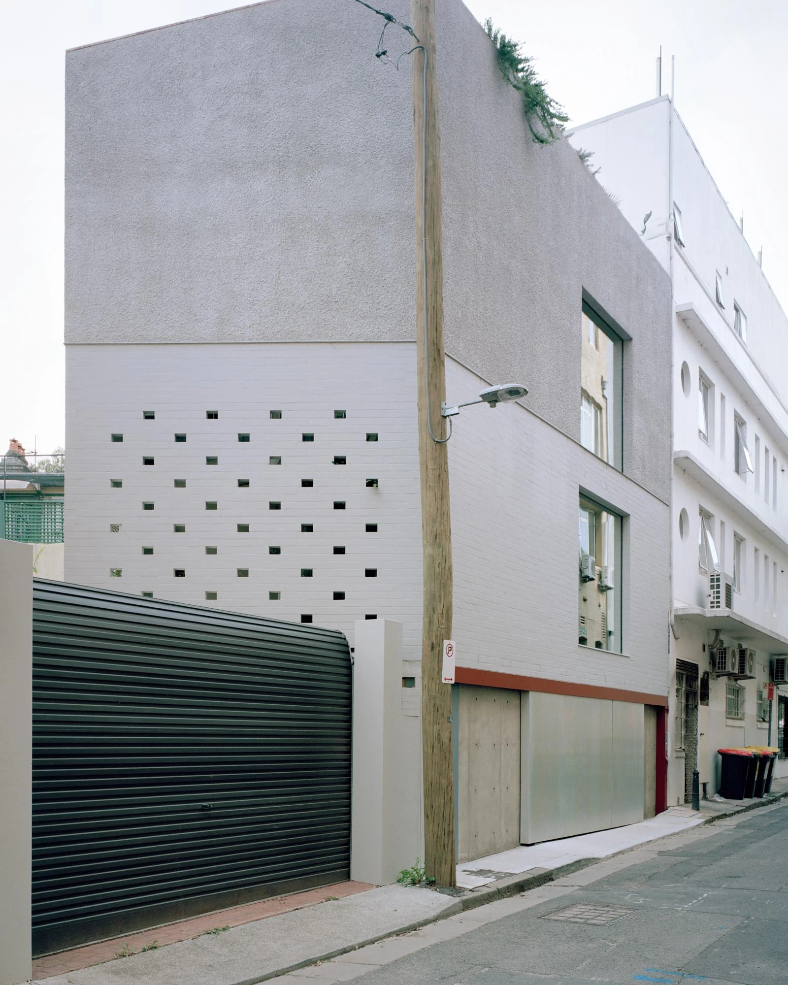 House next to Taylor Square by Anthony Gill Architects, photographed by Rory Gardiner with Colby Vexler — Corner view of the side elevation, perforated brick in a grid of square voids beside a dark green roller shutter.