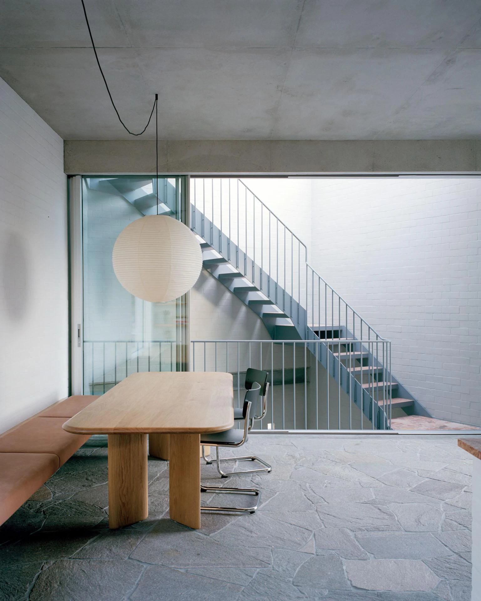 House next to Taylor Square by Anthony Gill Architects, photographed by Rory Gardiner with Colby Vexler — Dining area on irregular flagstone, a timber table and paper globe pendant, sliding glass open to the outdoor stair.