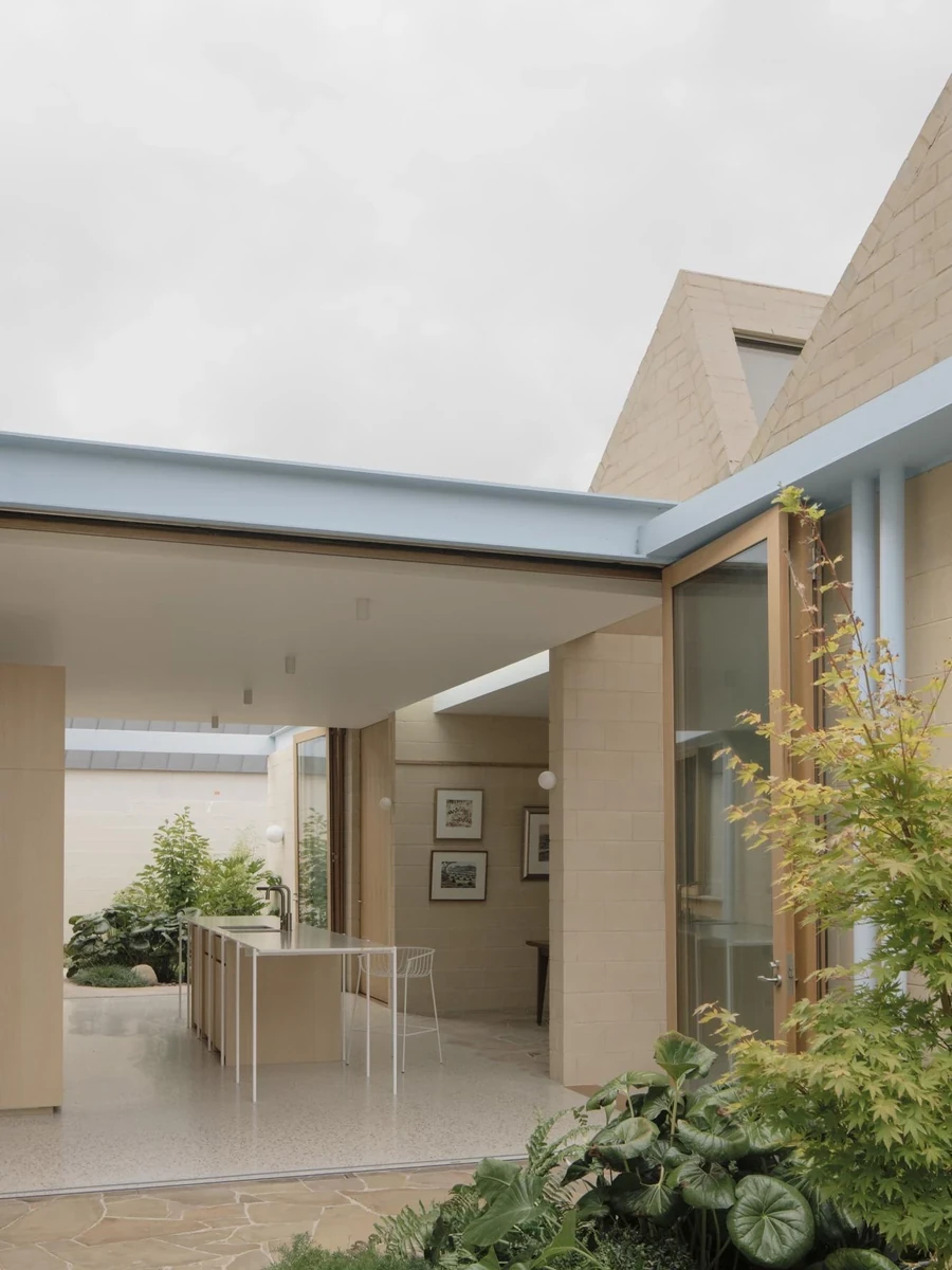 A Courtyard House by Office MIJI, photographed by Ben Hosking — the garden courtyard with a brick chimney, pale blue steel band and planted beds meeting a stone-paved path.