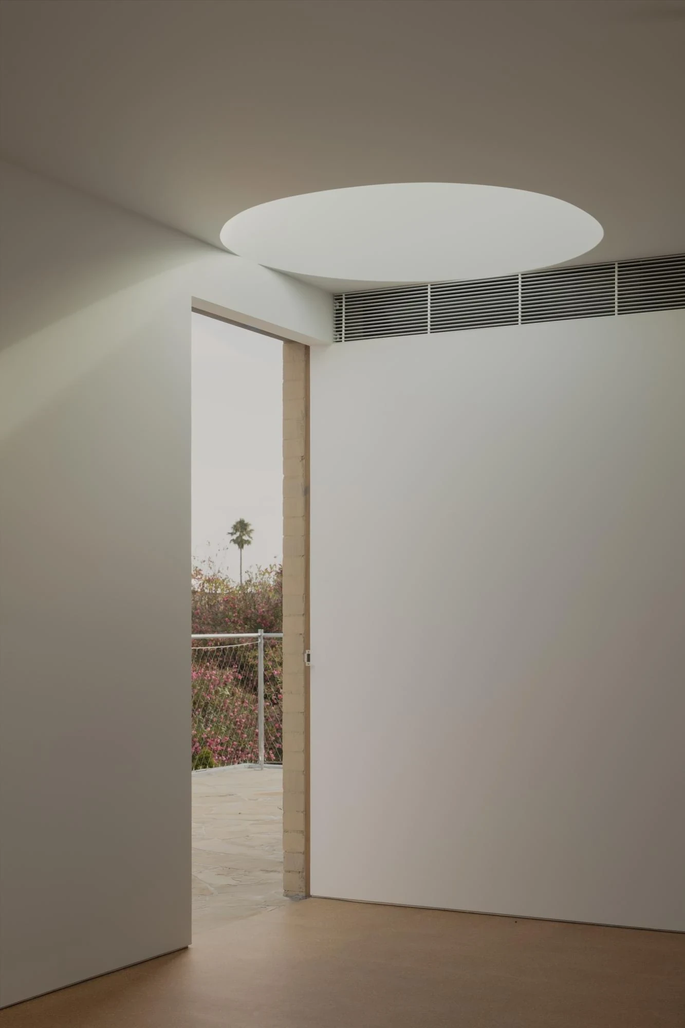 A Courtyard House by Office MIJI, photographed by Ben Hosking — an upstairs room with a circular ceiling oculus, a sliding door open past a brick jamb to a planted roof terrace.