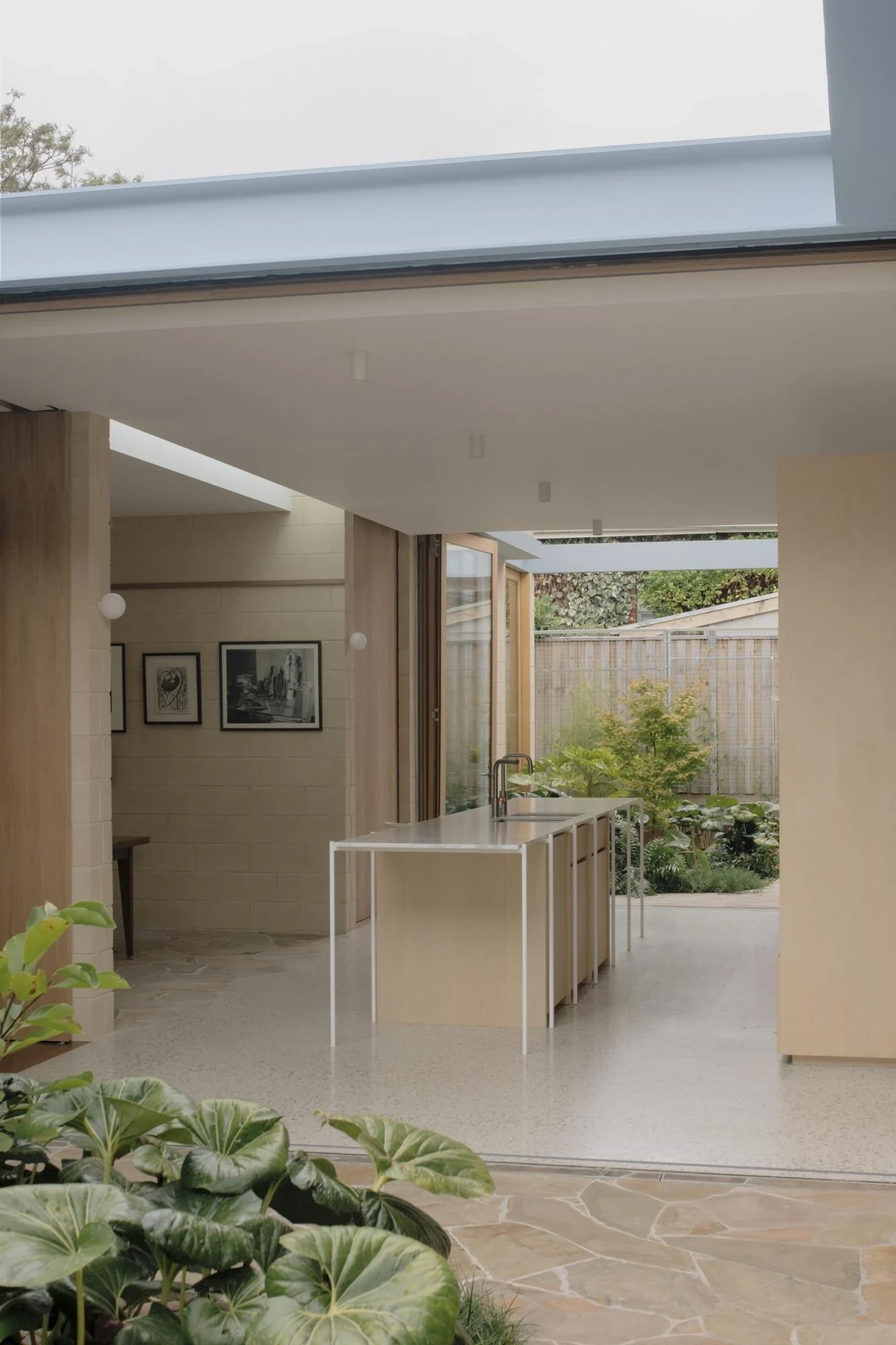 A Courtyard House by Office MIJI, photographed by Ben Hosking — the kitchen island floats on thin white legs on terrazzo, glass doors folded open to the courtyard garden.