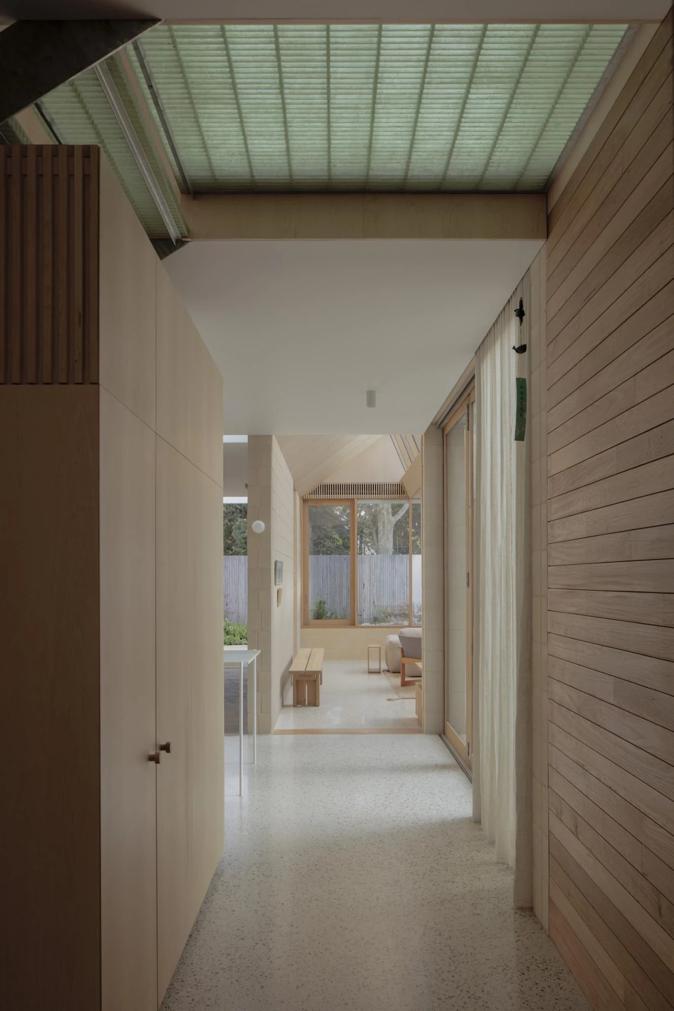 A Courtyard House by Office MIJI, photographed by Ben Hosking — a hallway lit from above by a green glass-block skylight, ash joinery on one side and timber-lined wall on the other.