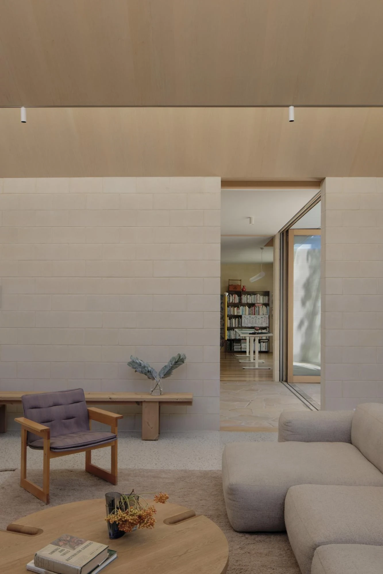 A Courtyard House by Office MIJI, photographed by Ben Hosking — a living room of white cement block and timber, a purple armchair and grey sofa on terrazzo, the study visible beyond.