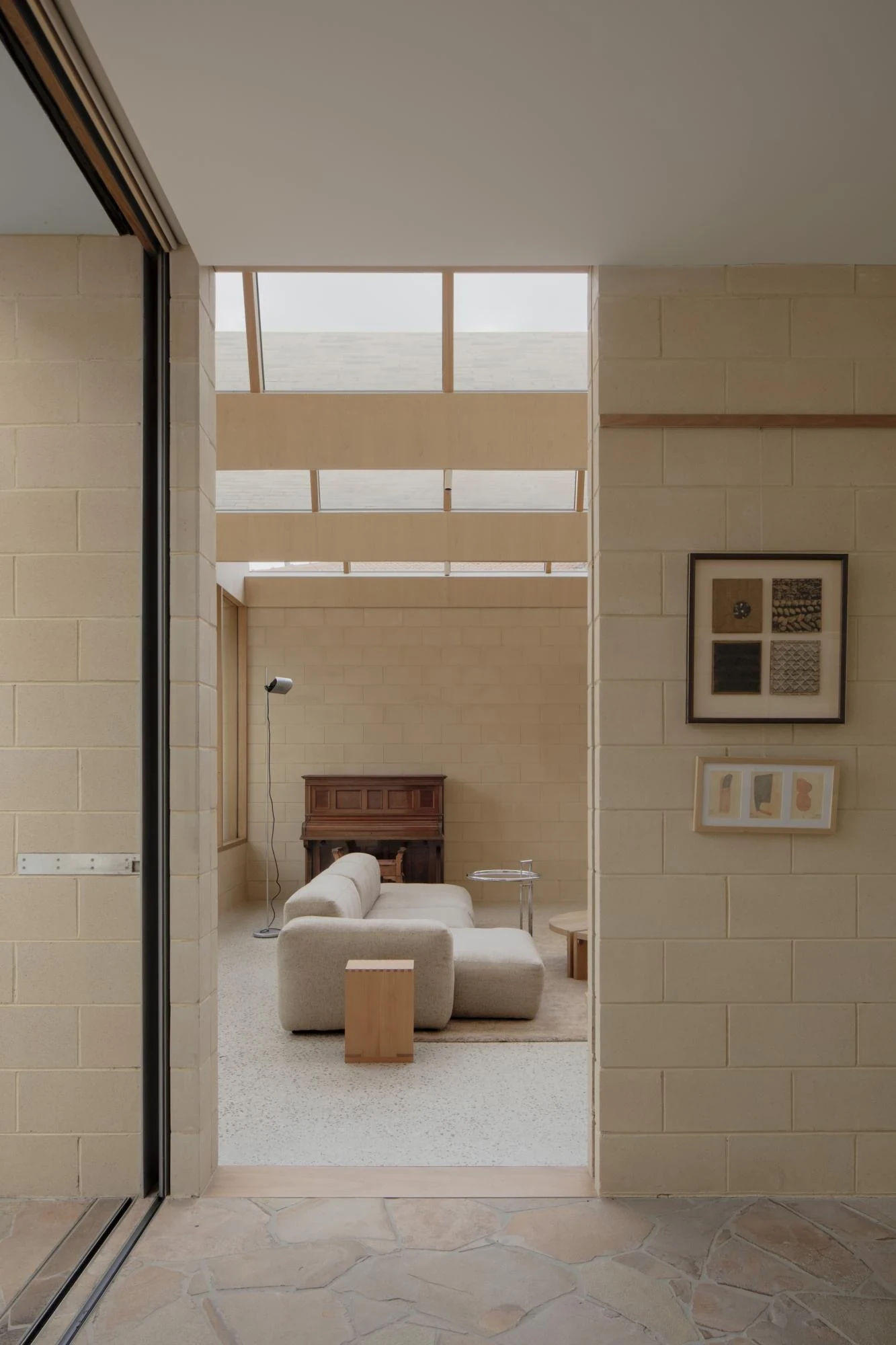 A Courtyard House by Office MIJI, photographed by Ben Hosking — a sitting quadrant seen through cement-block walls, an upper timber gallery admitting daylight above a dark upright piano.