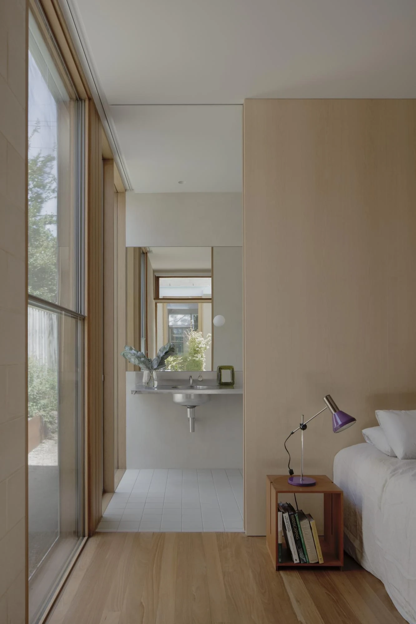 A Courtyard House by Office MIJI, photographed by Ben Hosking — a bedroom in ash and cement block opening to a stainless vanity and a courtyard view through the ensuite.
