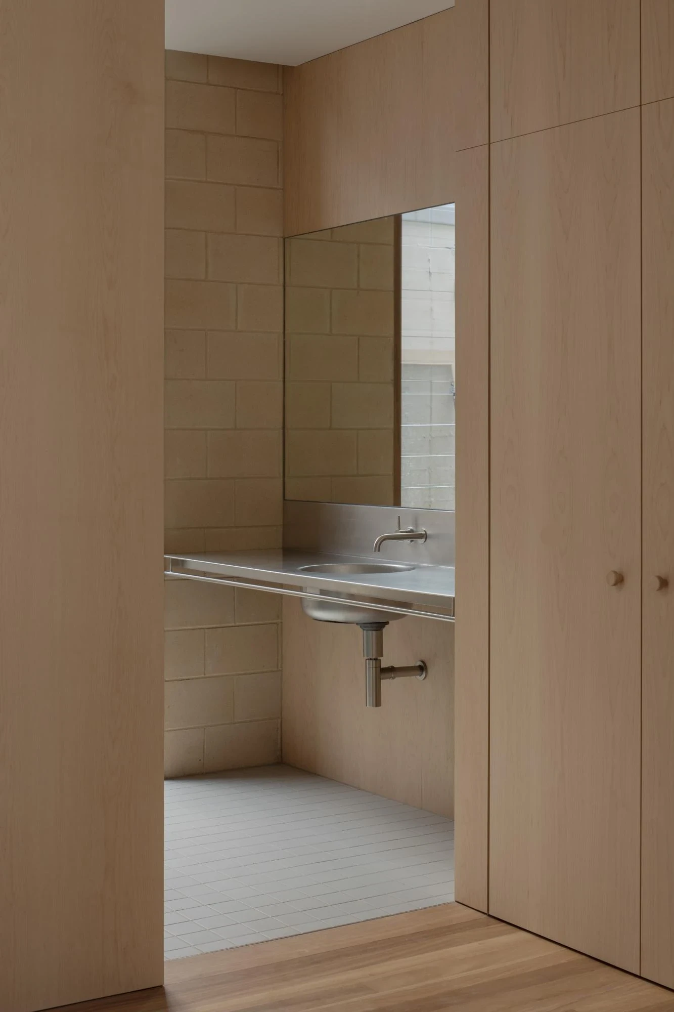 A Courtyard House by Office MIJI, photographed by Ben Hosking — a cement-block ensuite glimpsed between timber joinery, a stainless trough sink cantilevered above white-tiled floor.