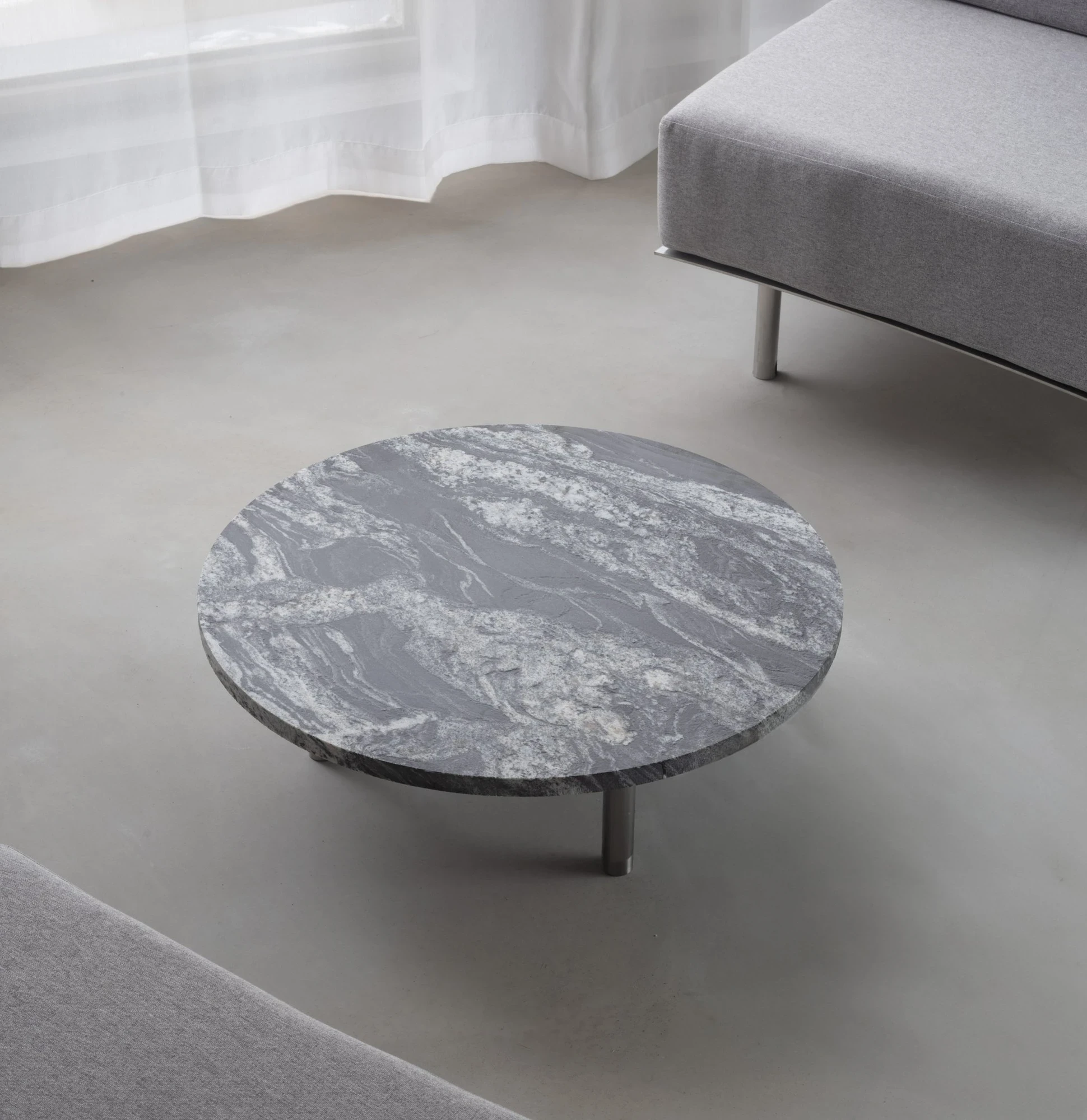 Ximen Apartment by unprofessional.studio, photographed by unprofessional.studio: the round grey marble coffee table with white veining set on the microcement floor beside the grey sofa.