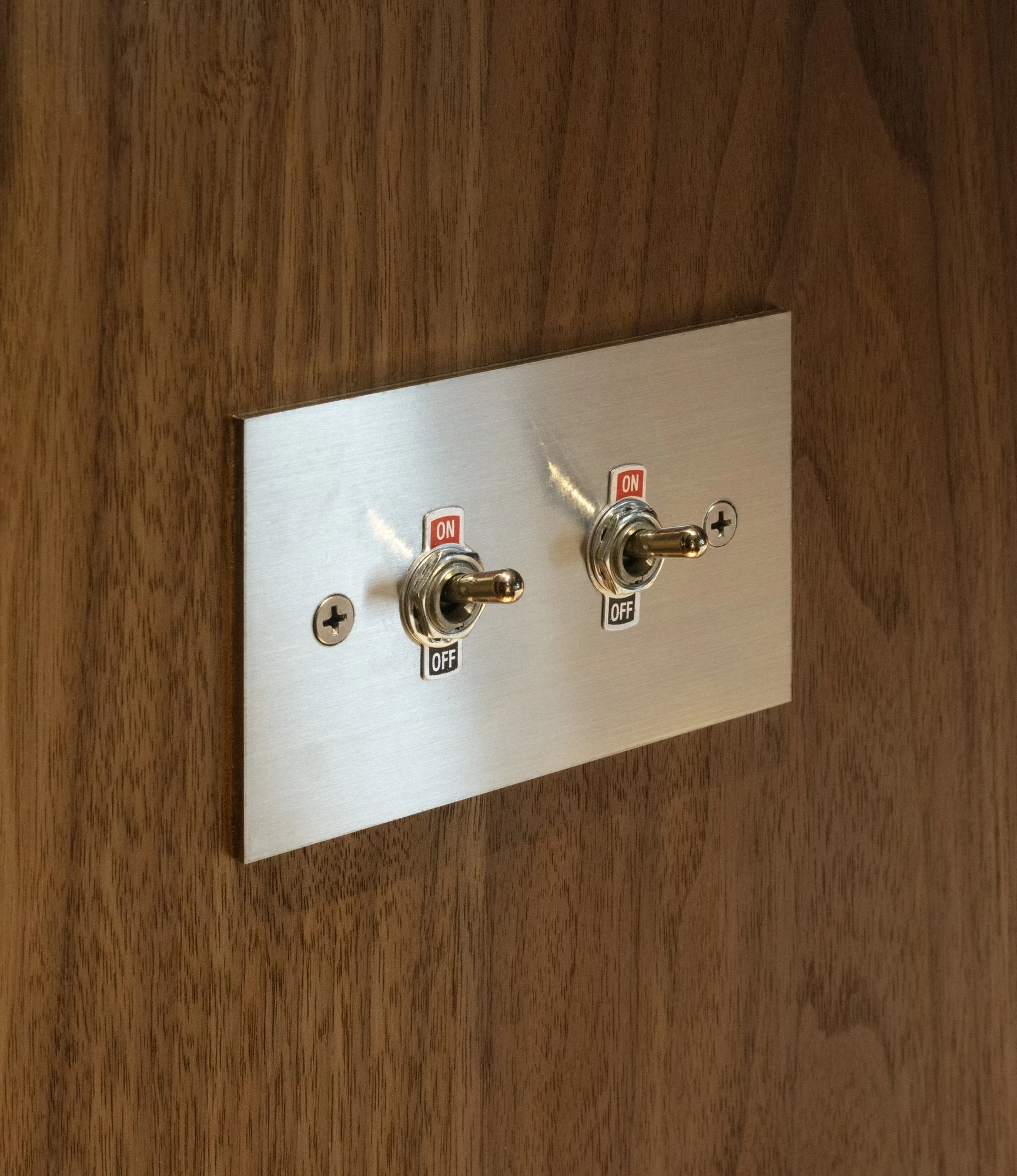 Ximen Apartment by unprofessional.studio, photographed by unprofessional.studio: brushed stainless steel toggle switches set into a walnut panel, a detail foregrounding the fittings.