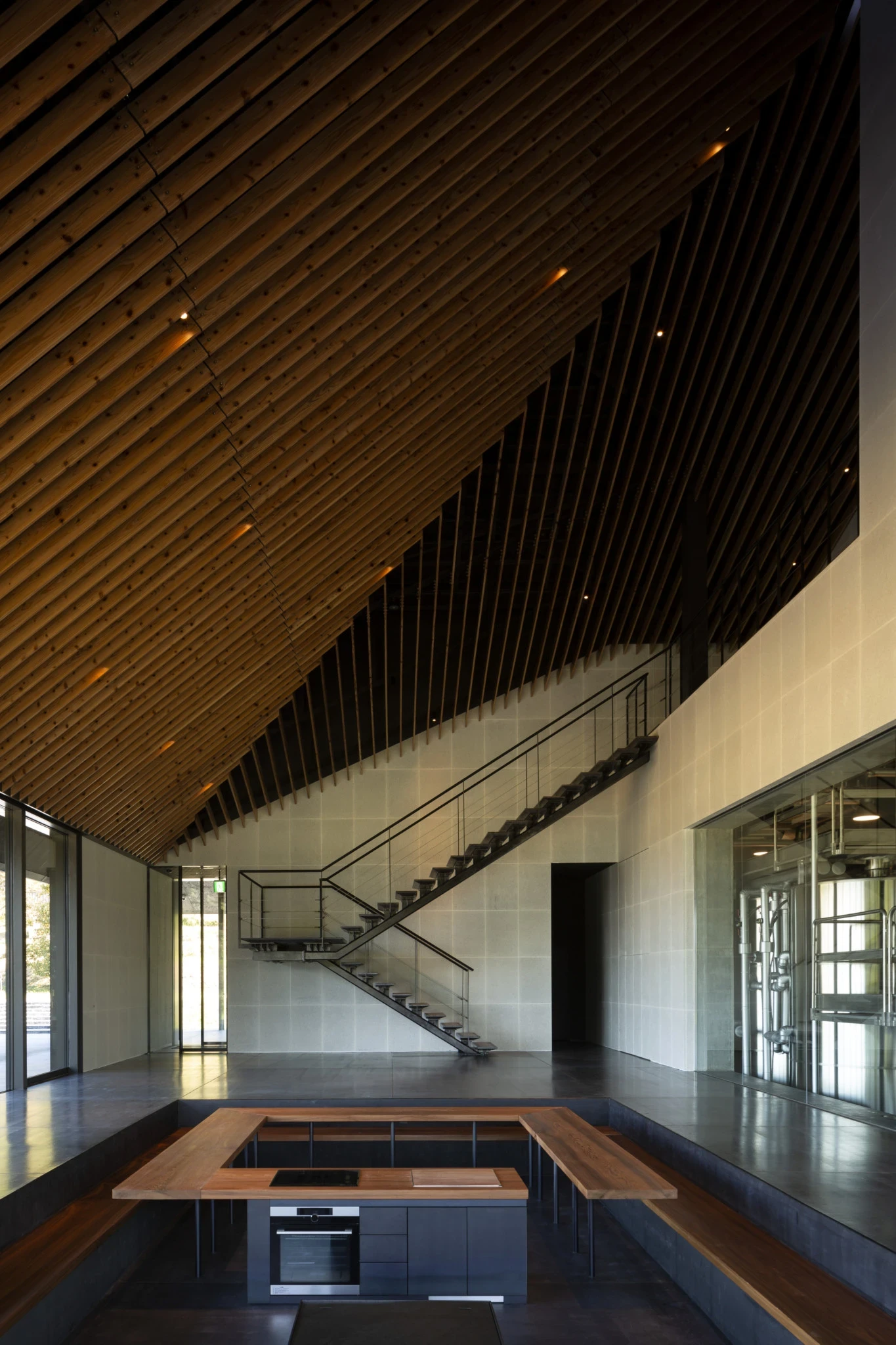 IWA Sake Brewery by Kengo Kuma & Associates, photographed by Mitsumasa Fujitsuka — The sugi cedar ceiling rakes steeply up the roofline over the reception hall, a slender steel stair climbing a pale masonry wall