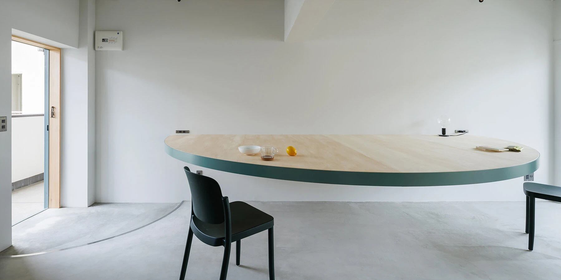 A Large Semicircle That Holds Everyday Life by Tato Architects, photographed by Yohei Sasakura: the table in full profile from the balcony side, its arc echoed by a shadow cast across the polished concrete floor.