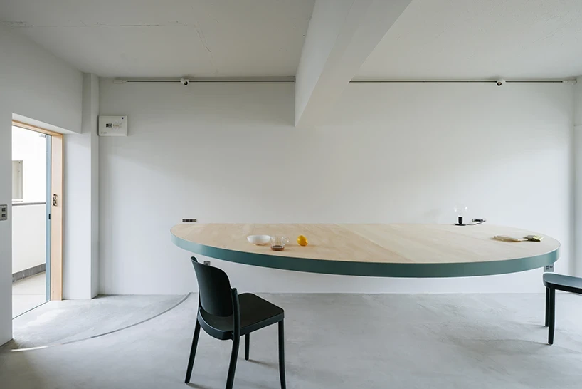 A Large Semicircle That Holds Everyday Life by Tato Architects, photographed by Yohei Sasakura: the semicircular table floats in the white room, two dark chairs and breakfast items at its curved front and straight wall edge.