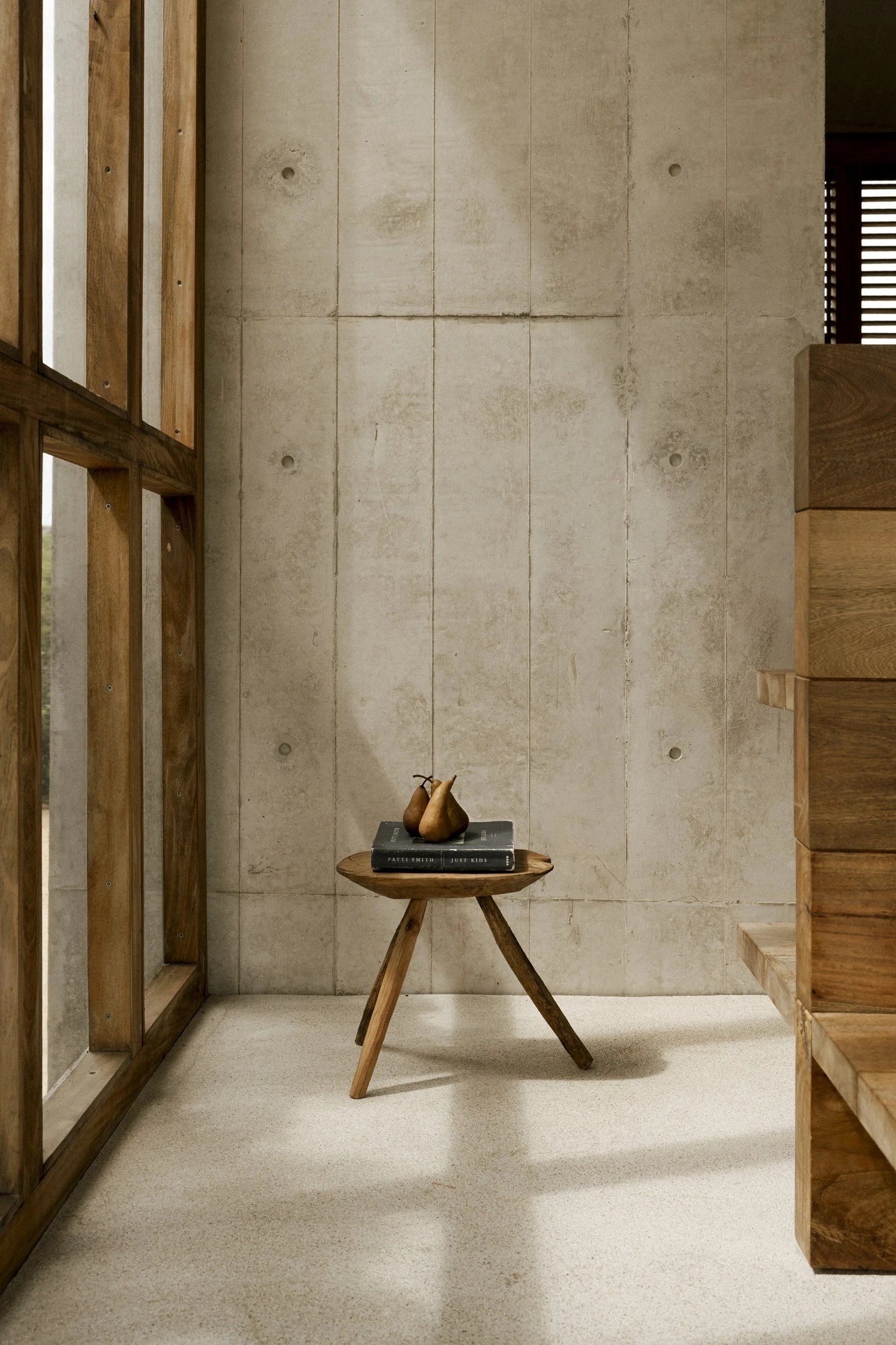 Casa Viento by Aranza De Ariño, photographed by Diego Orvaños — a three-legged timber stool holds pears and a book against a board-formed concrete wall and terrazzo floor.