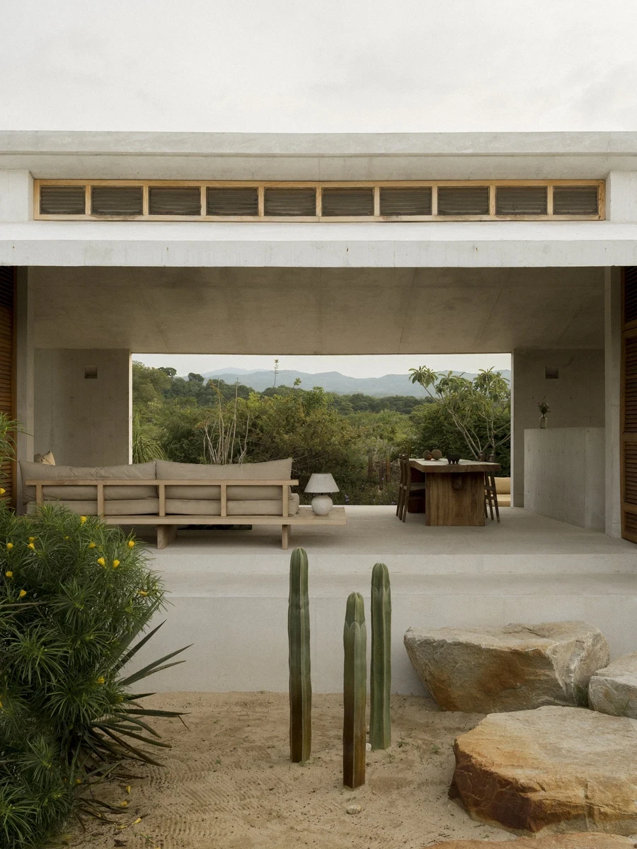 Casa Viento by Aranza De Ariño, photographed by Diego Orvaños — the open living pavilion frames a timber sofa and dining table against distant mountains, cactus in the sand foreground.