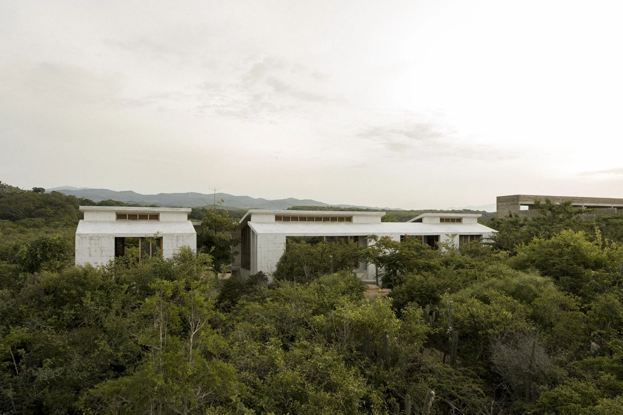 Casa Viento by Aranza De Ariño, photographed by Diego Orvaños — the full three-volume plan reads across the scrub, the open central pavilion visible through the trees.