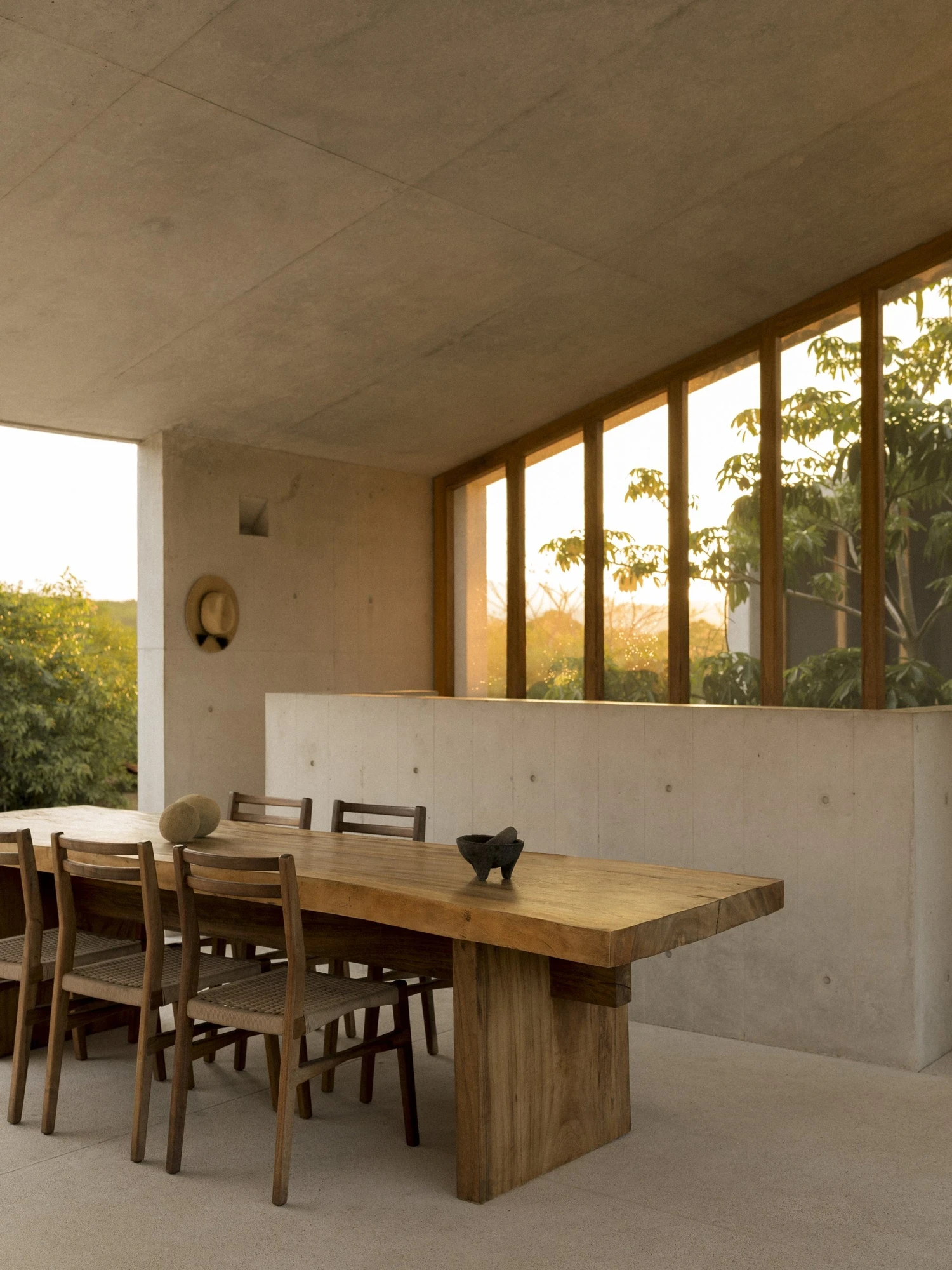 Casa Viento by Aranza De Ariño, photographed by Diego Orvaños — warm evening light floods the dining pavilion, a straw hat on the concrete wall above the timber table.