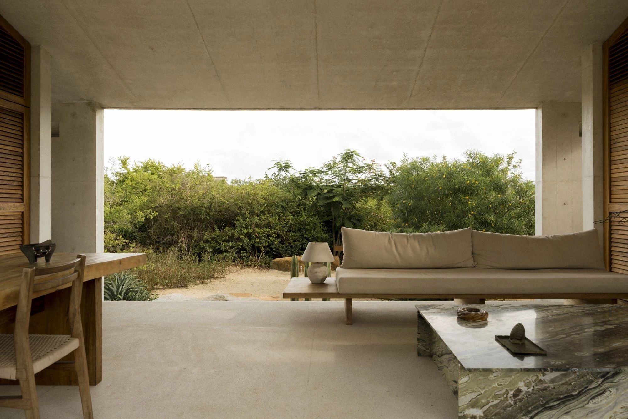 Casa Viento by Aranza De Ariño, photographed by Diego Orvaños — the living pavilion opens fully to flowering scrub, low daybed and marble table on pale terrazzo.