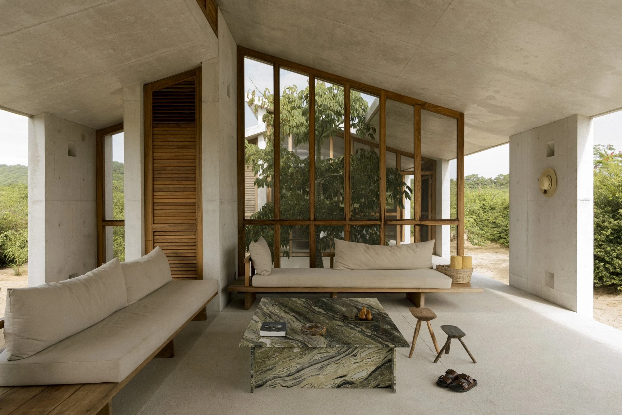 Casa Viento by Aranza De Ariño, photographed by Diego Orvaños — a linen daybed and a green-veined marble block sit under the concrete soffit, a glazed pavilion across the terrace.