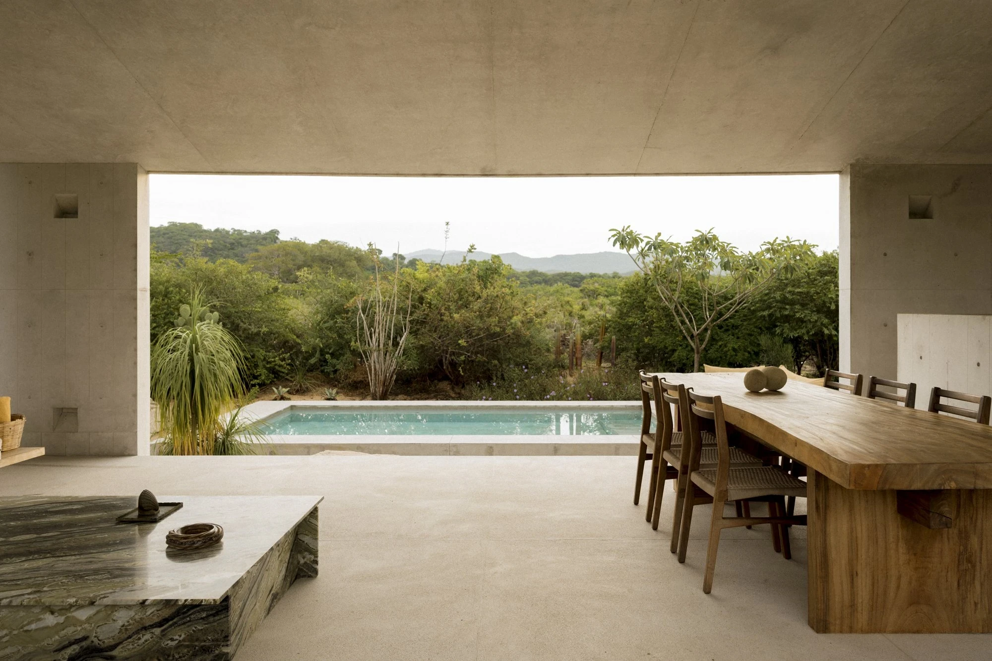 Casa Viento by Aranza De Ariño, photographed by Diego Orvaños — the lap pool sits framed in the pavilion opening beside a live-edge timber table, mountains beyond.