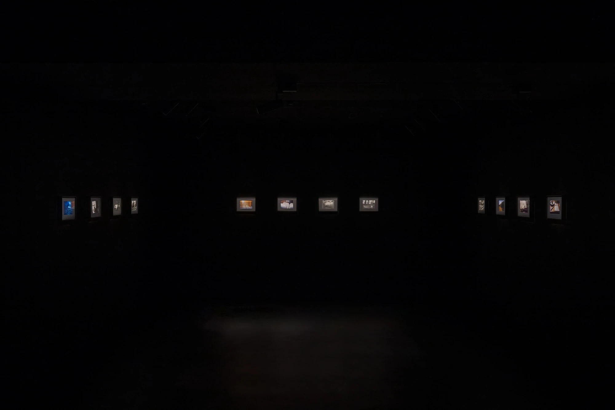 Spillover by Ann Zhao, photographed by Felix S.C. Wong — A wall of small framed photographs floats as lit windows across the darkness of the nineteenth floor installation