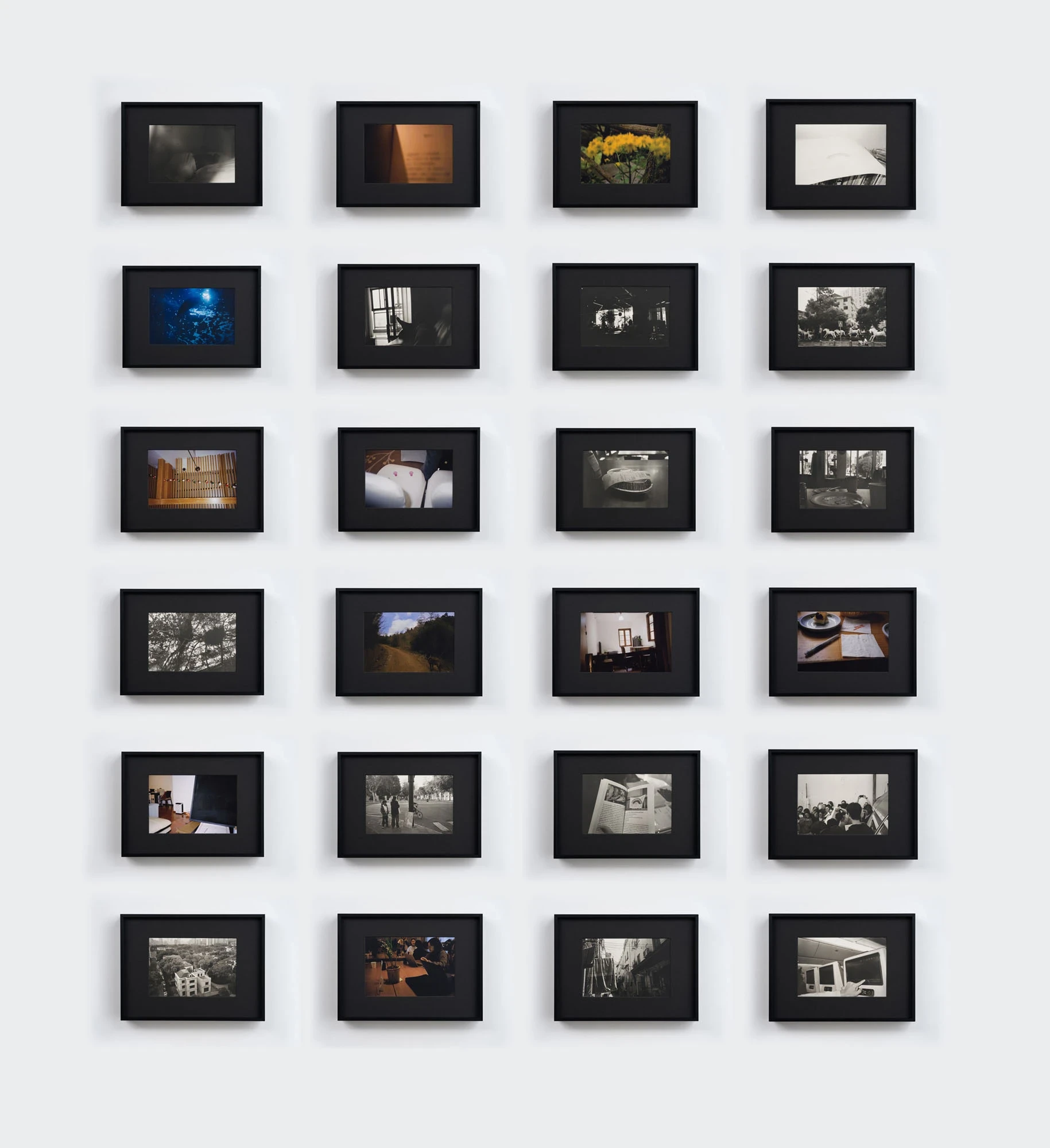 Spillover by Ann Zhao, photographed by Felix S.C. Wong — The full grid of twenty-four framed photographs arranged in six rows on a white wall, alternating black-and-white and muted colour images