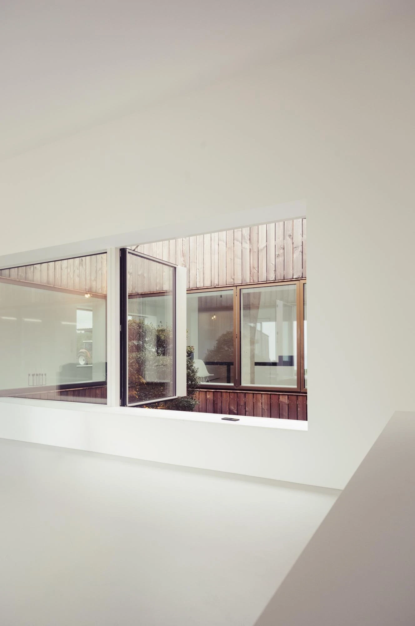 Barnhouse in Berau by Klaus Keller Andy Keller Kathrin Keller Architekten, photographed by Andy Keller — A view down into the timber-lined courtyard through an interior window set in a white wall, one casement swung open