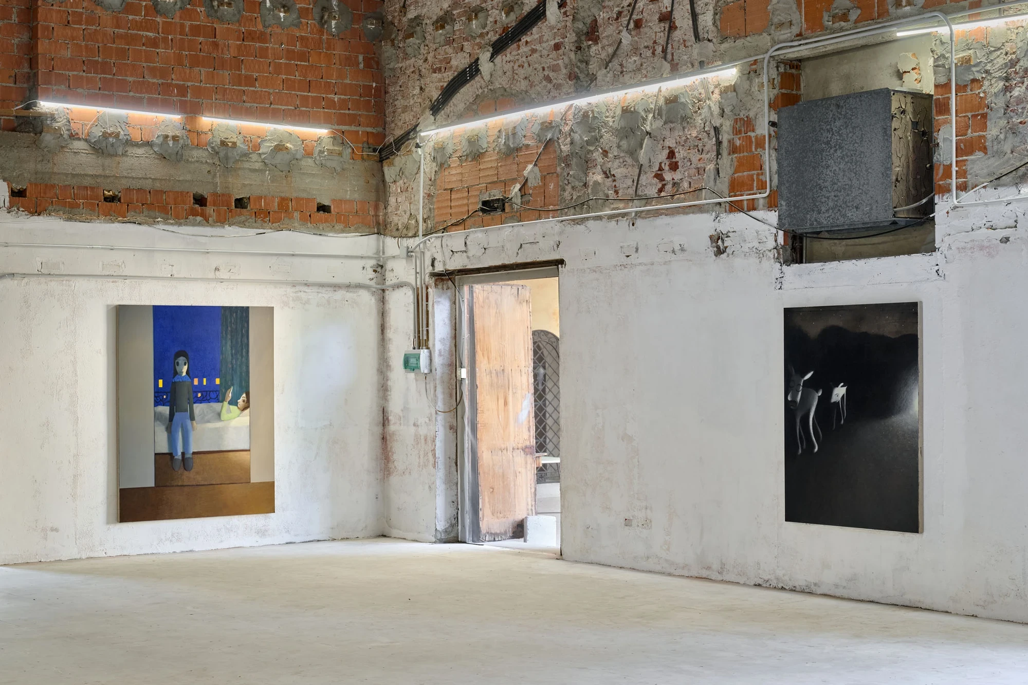 Every Day, Mostly Night, Sometimes Daylight by Satoru Kurata, photographed by Michela Pedranti -- A corner of the hall under a high brick wall and metal duct, a night bedroom painting on the left and a black night-landscape canvas on the right, an open we