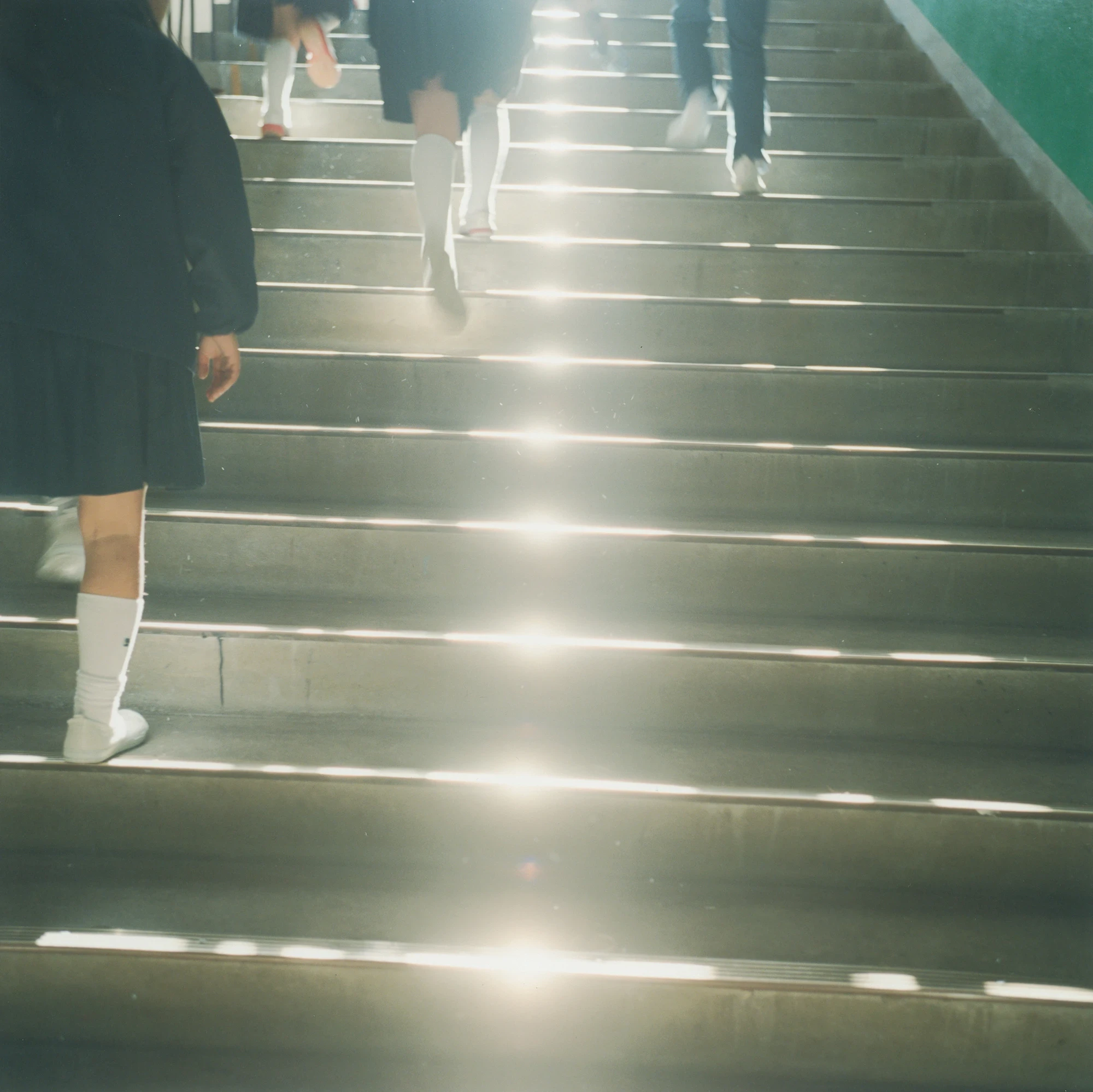 Illuminance by Rinko Kawauchi -- Students descend a sunlit stairwell, the light striping the steps horizontally