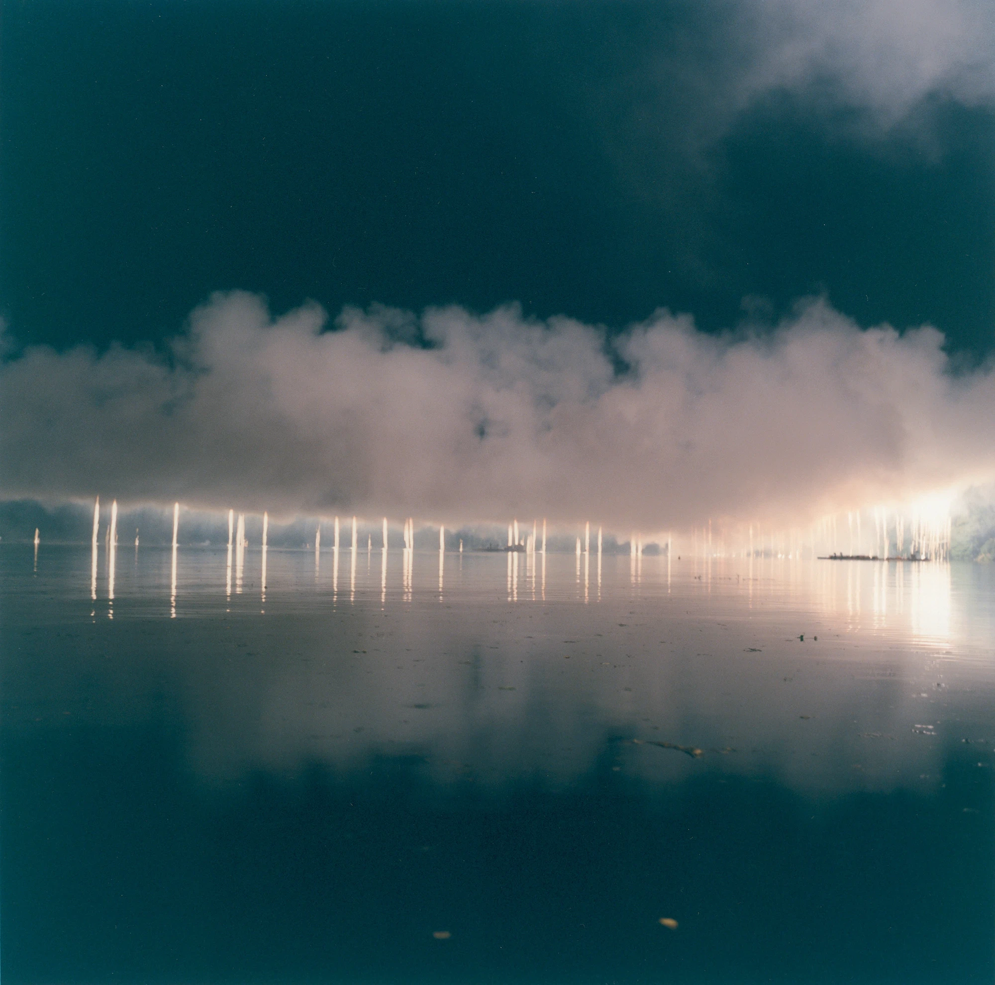 Illuminance by Rinko Kawauchi -- Strings of light reflect on still water beneath a bank of low cloud at night