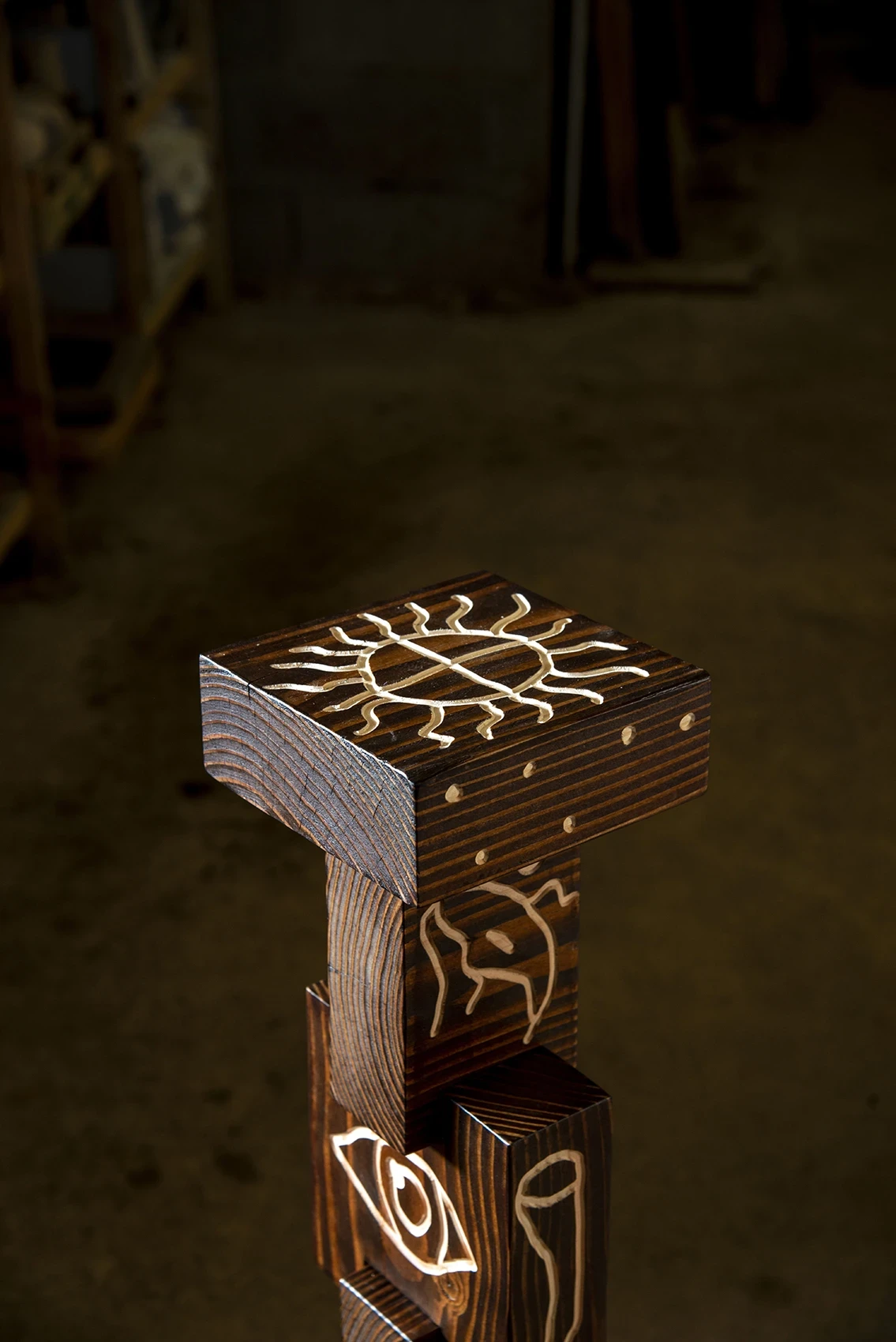 Les Rhizopodes by Barreau Charbonnet — Detail of a stacked totem's top block, a radiating sun motif filled pale cream, an eye emerging on the block below