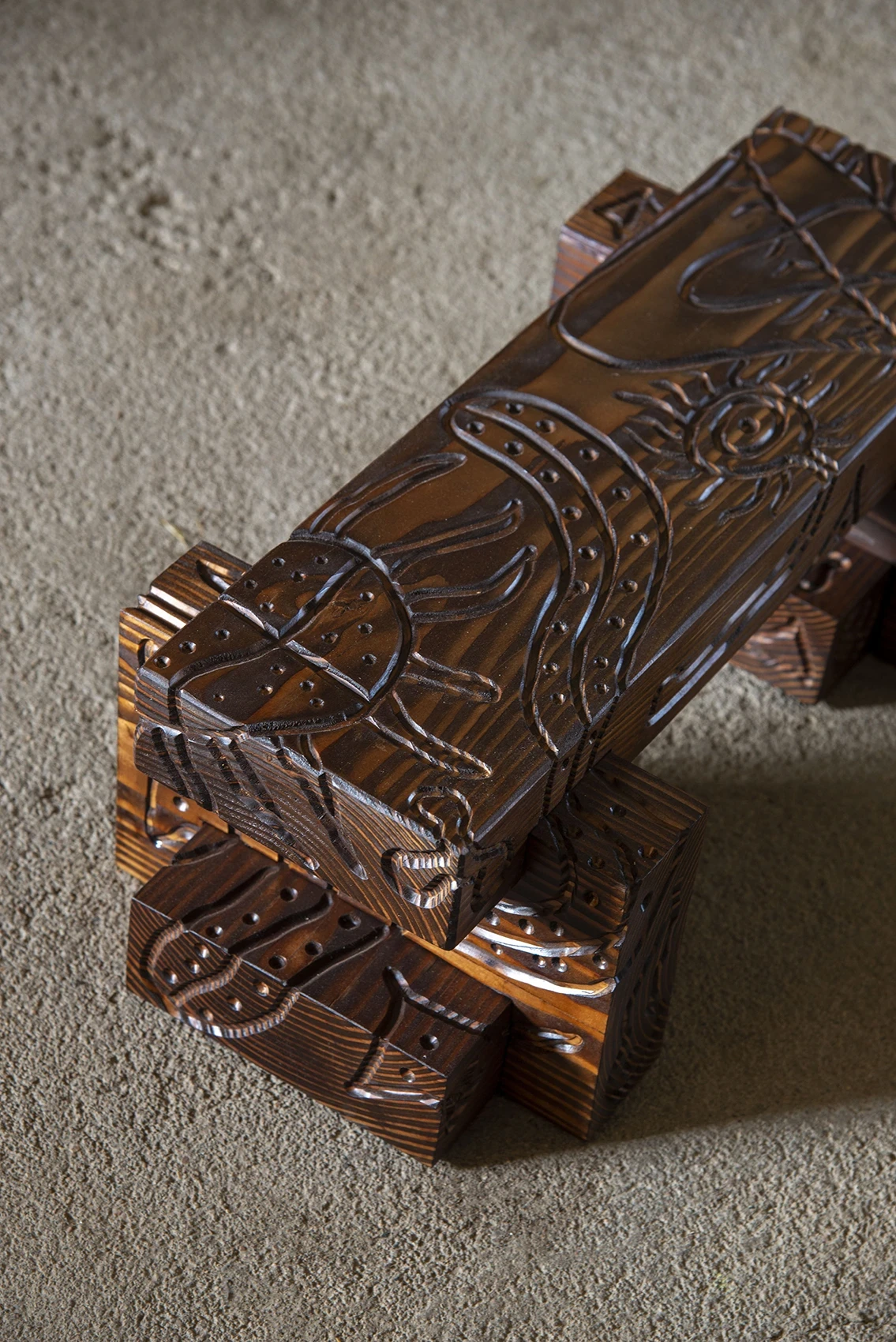 Les Rhizopodes by Barreau Charbonnet — Overhead view of a small carved bench, sun and spider forms left in bare warm wood