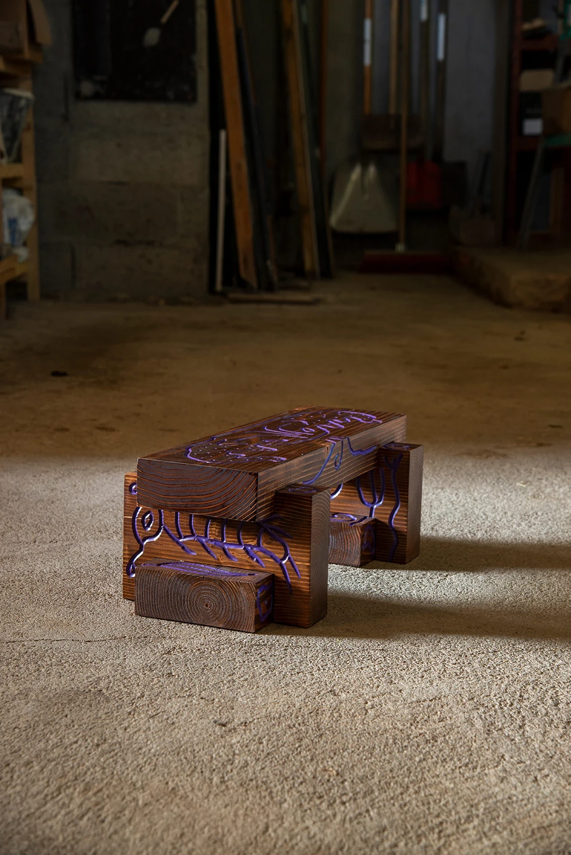 Les Rhizopodes by Barreau Charbonnet — A low bench in warm timber on the workshop floor, an amoeba-like body and trailing filaments filled bright violet