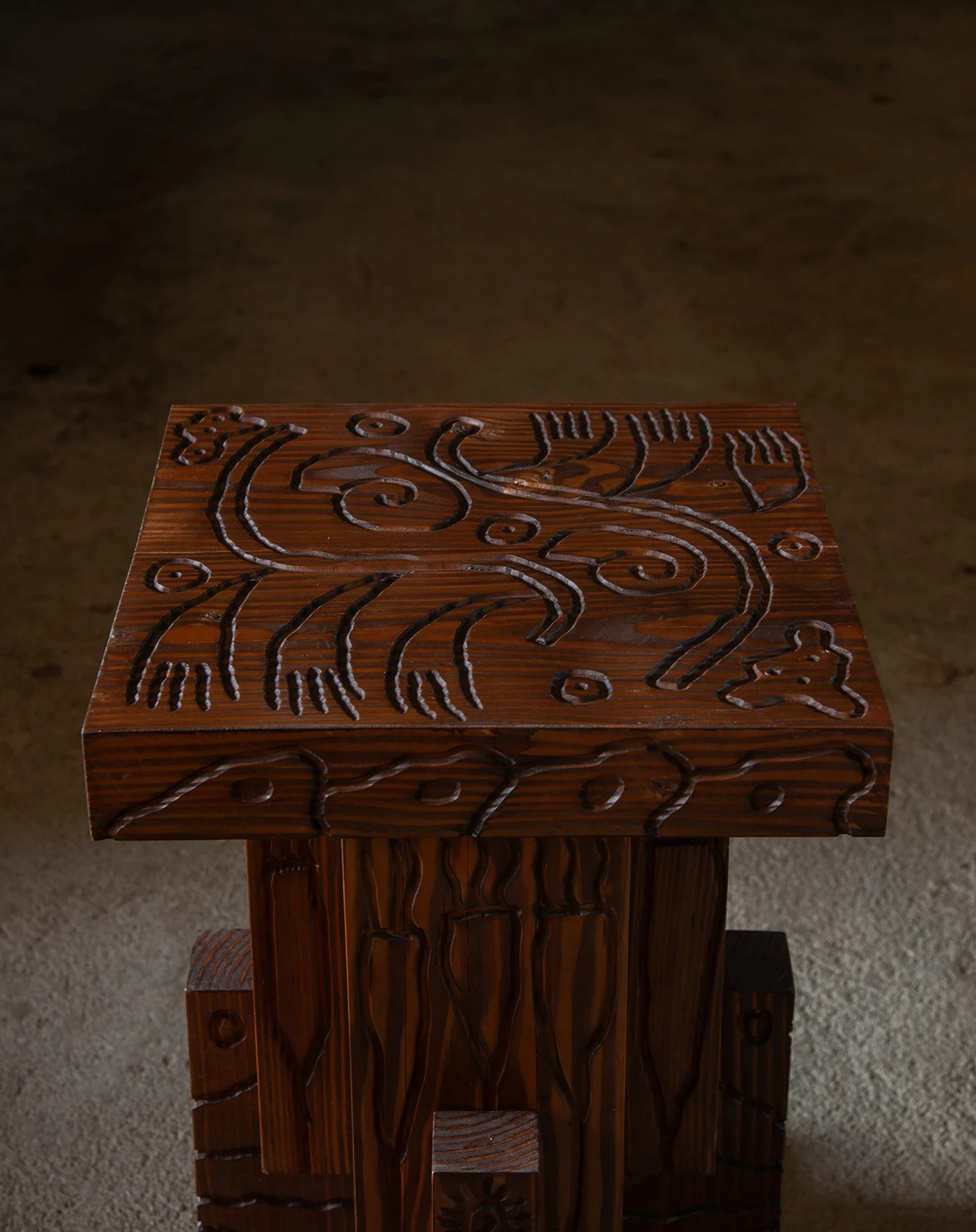 Les Rhizopodes by Barreau Charbonnet — Overhead detail of a square tabletop, spirals and fern-like strokes cut straight into warm reddish grain and left unpainted