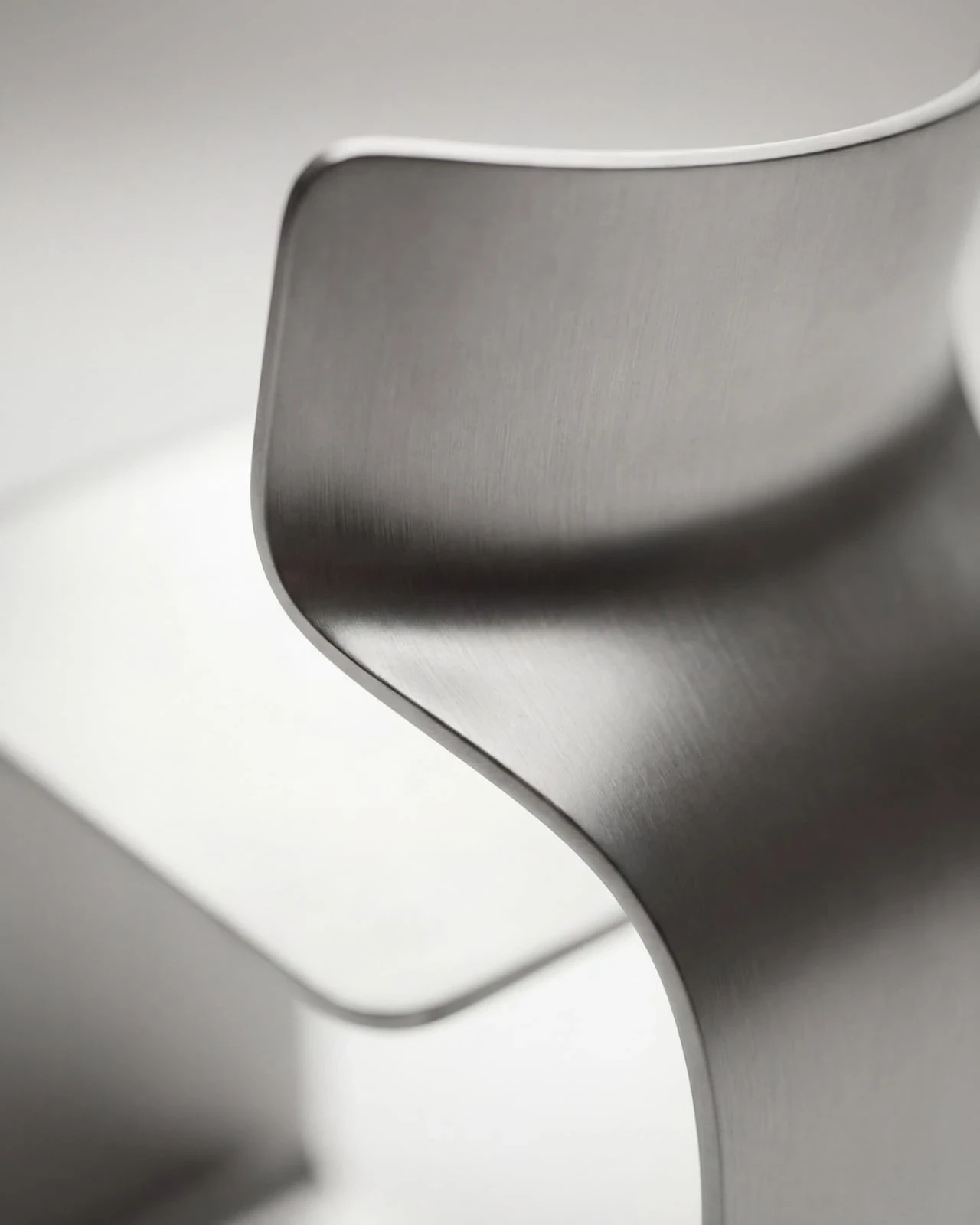 ZERO Chair by Davide Bozzo — An extreme close-up of the transition from seat to backrest, the brushed grain of the metal reading as fine parallel lines across the curved shell