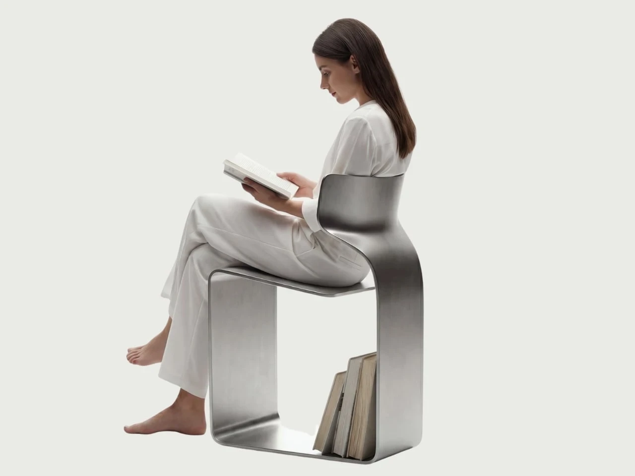 ZERO Chair by Davide Bozzo — A model in white sits on the chair reading, bare feet resting on the pale floor, a few books slotted into the open rectangle of the base below the seat