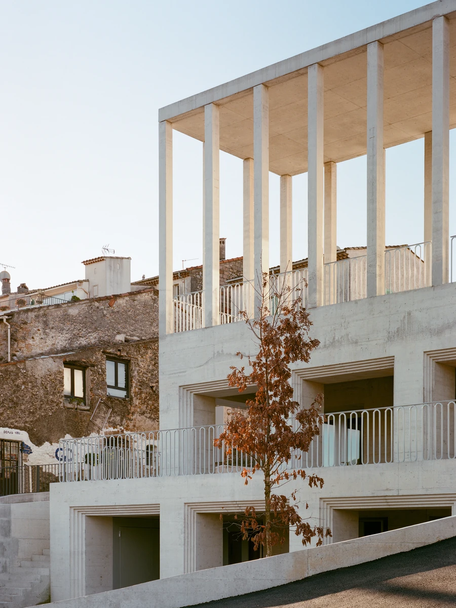 Biot Municipal Building Extension by Atelier EGR, photographed by Giaime Meloni — Angled view of the columned terrace above deep openings, with an old rendered stone wall and a young oak alongside.
